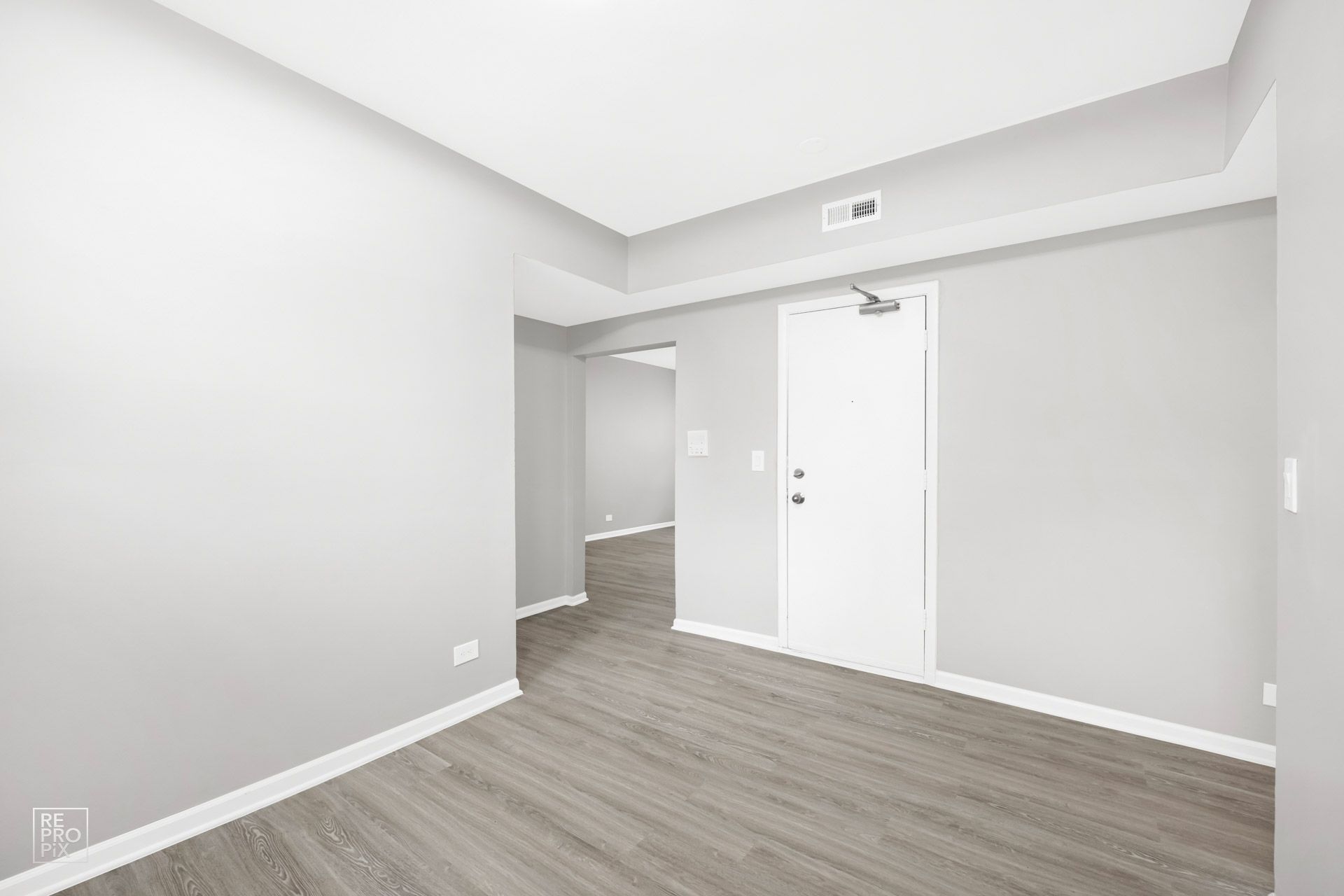 Empty room with gray walls and flooring, white door, and hallway entrance.