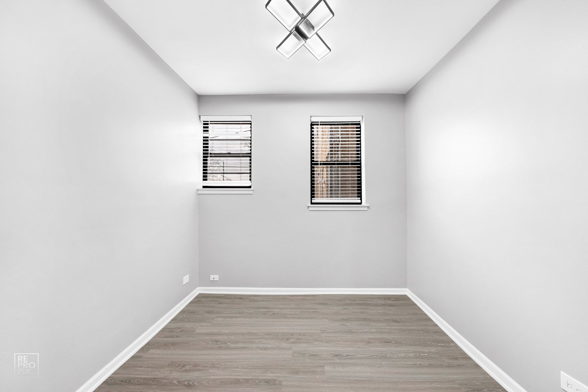 Empty, gray-painted room with two windows, a light fixture, and wood-look flooring.