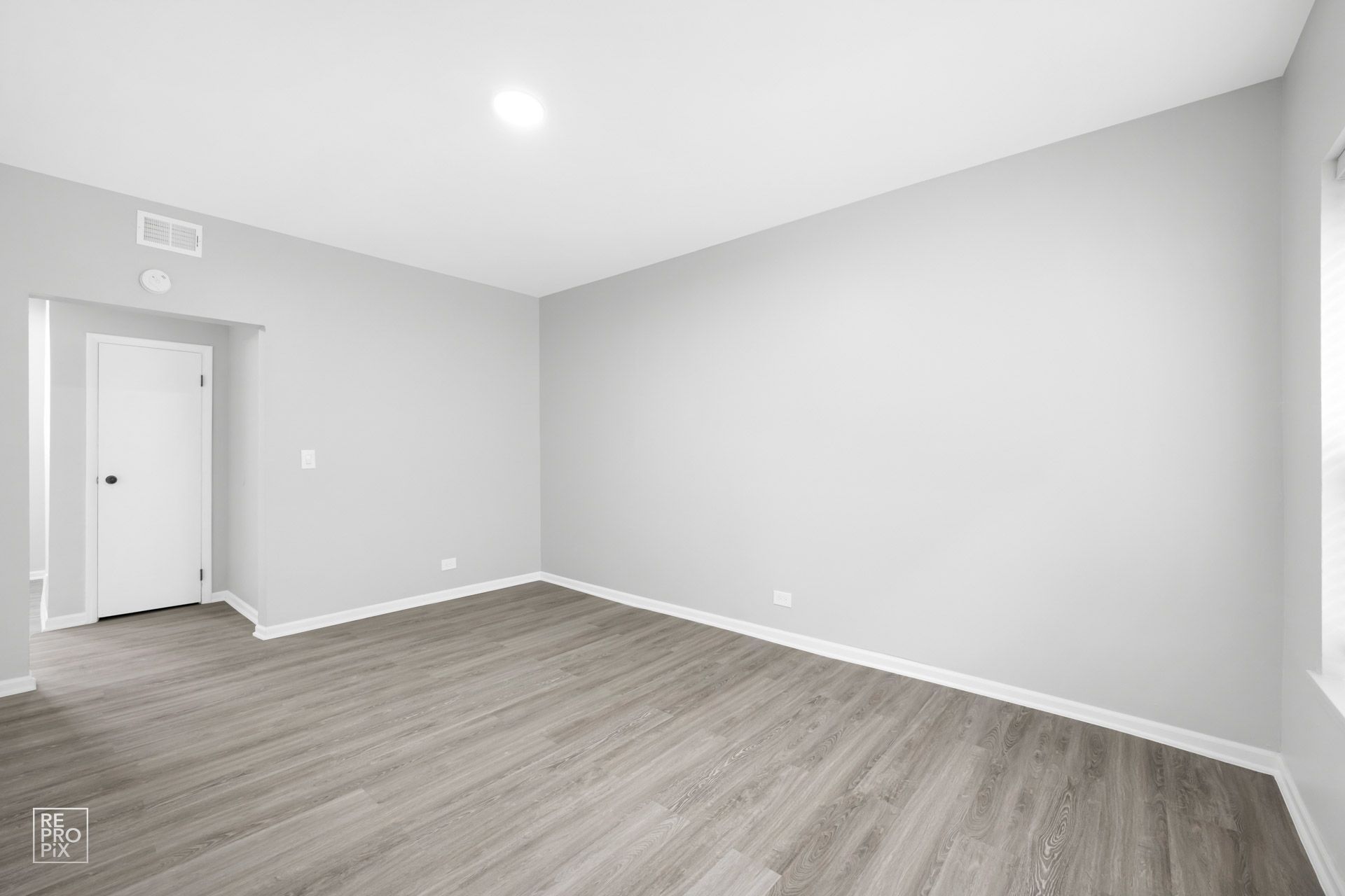 Empty room with light gray walls, wood-look flooring, and a closed white door.