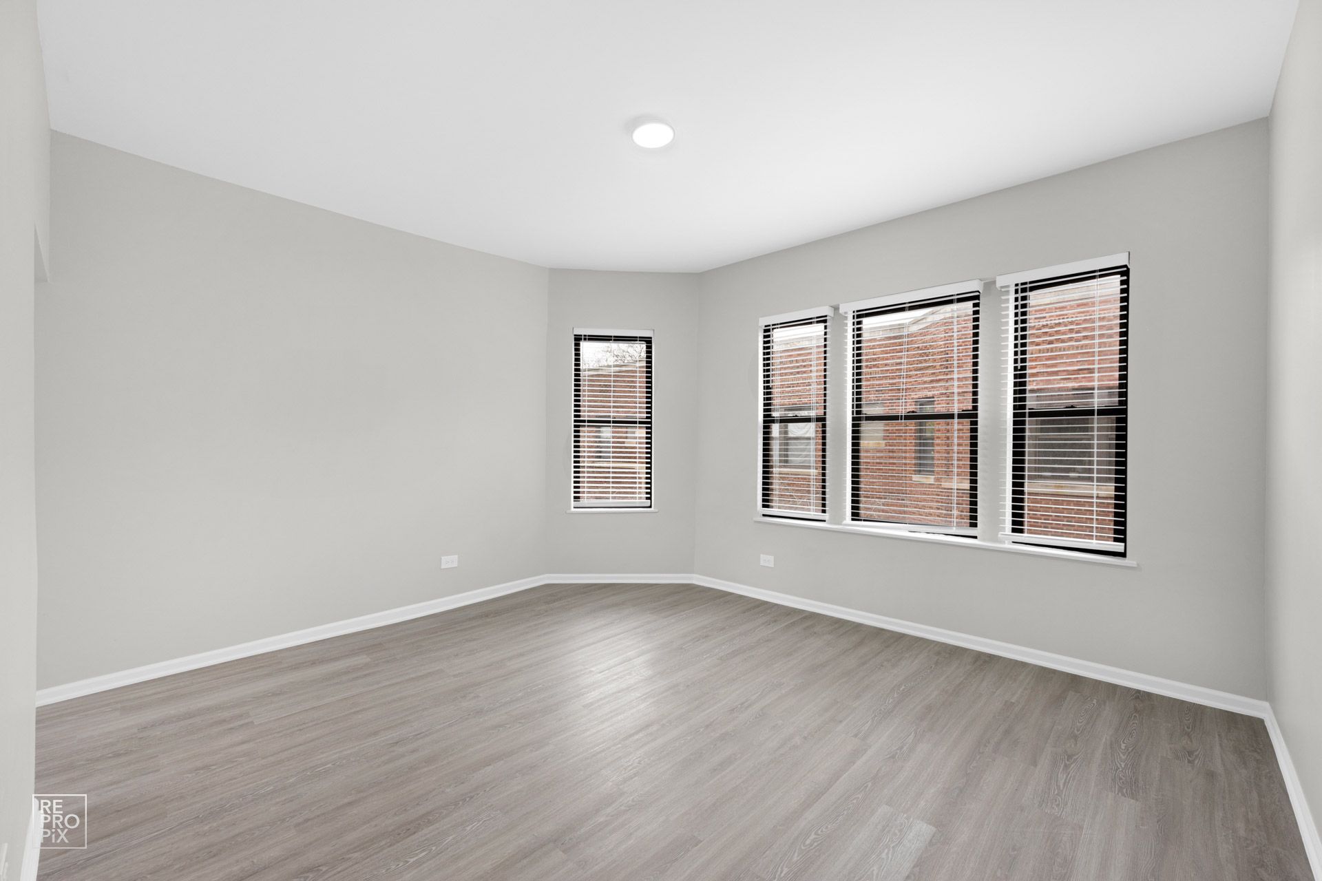 Empty room with light gray walls, gray wood-look floor, and three windows with blinds.