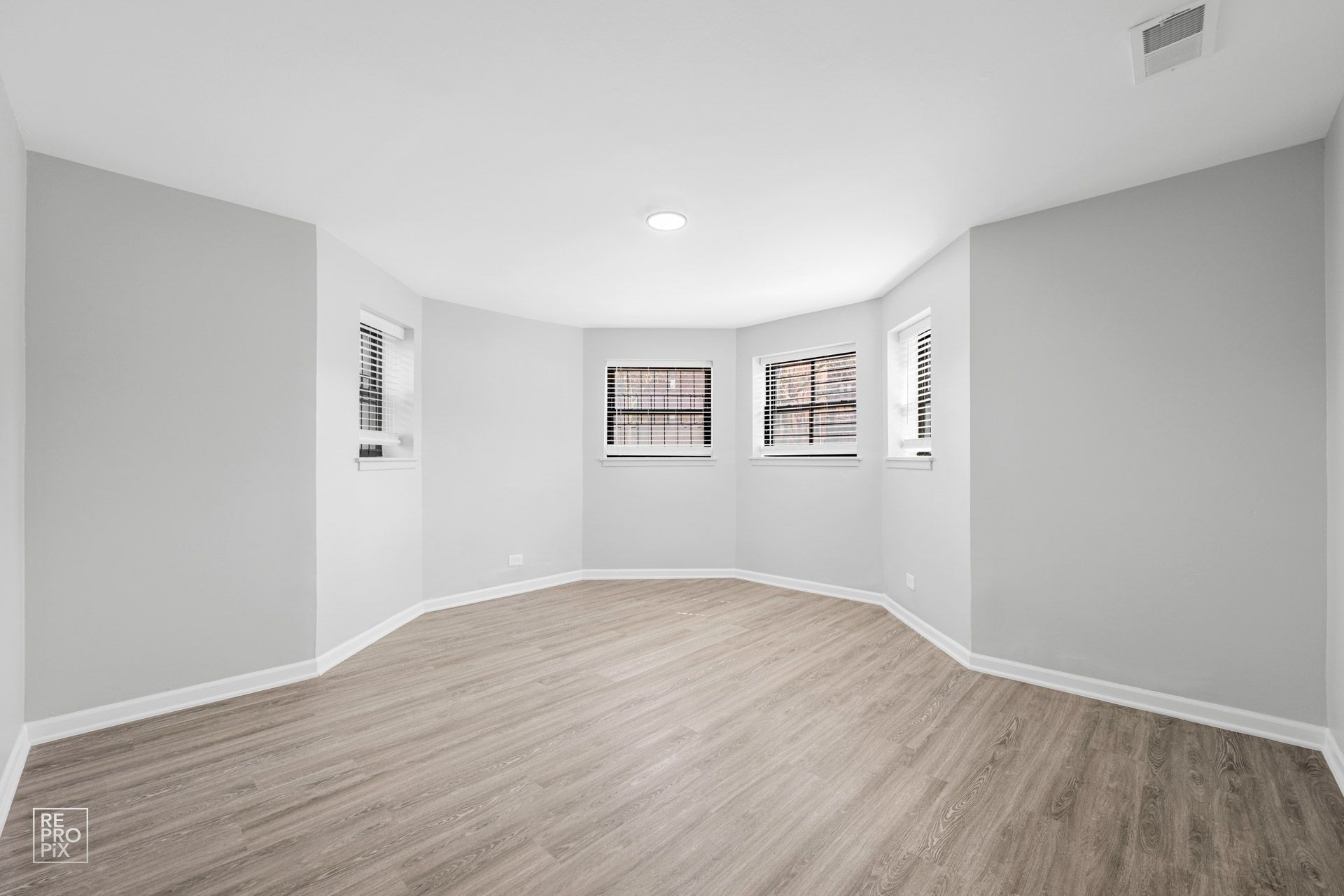 Empty, light-grey-walled room with wooden floor and three windows on the curved wall.