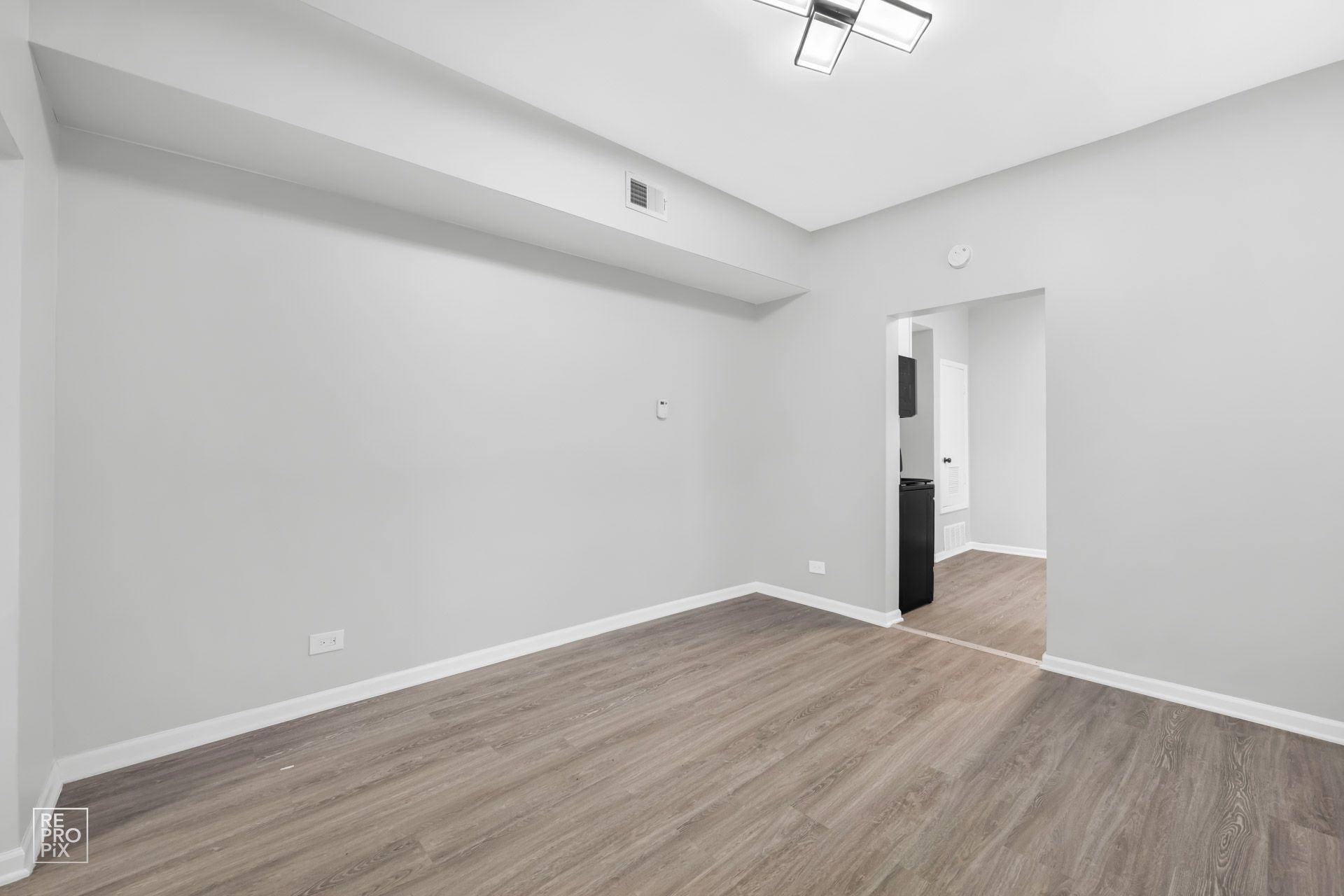 Empty room with gray walls and wood-look flooring. An opening leads to another area.