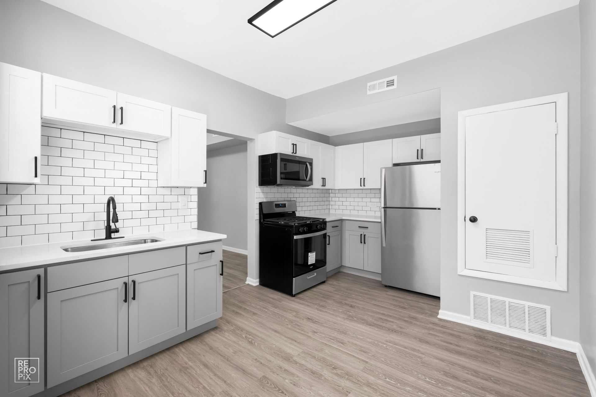 Modern kitchen with gray and white cabinets, stainless steel appliances, and light wood flooring.