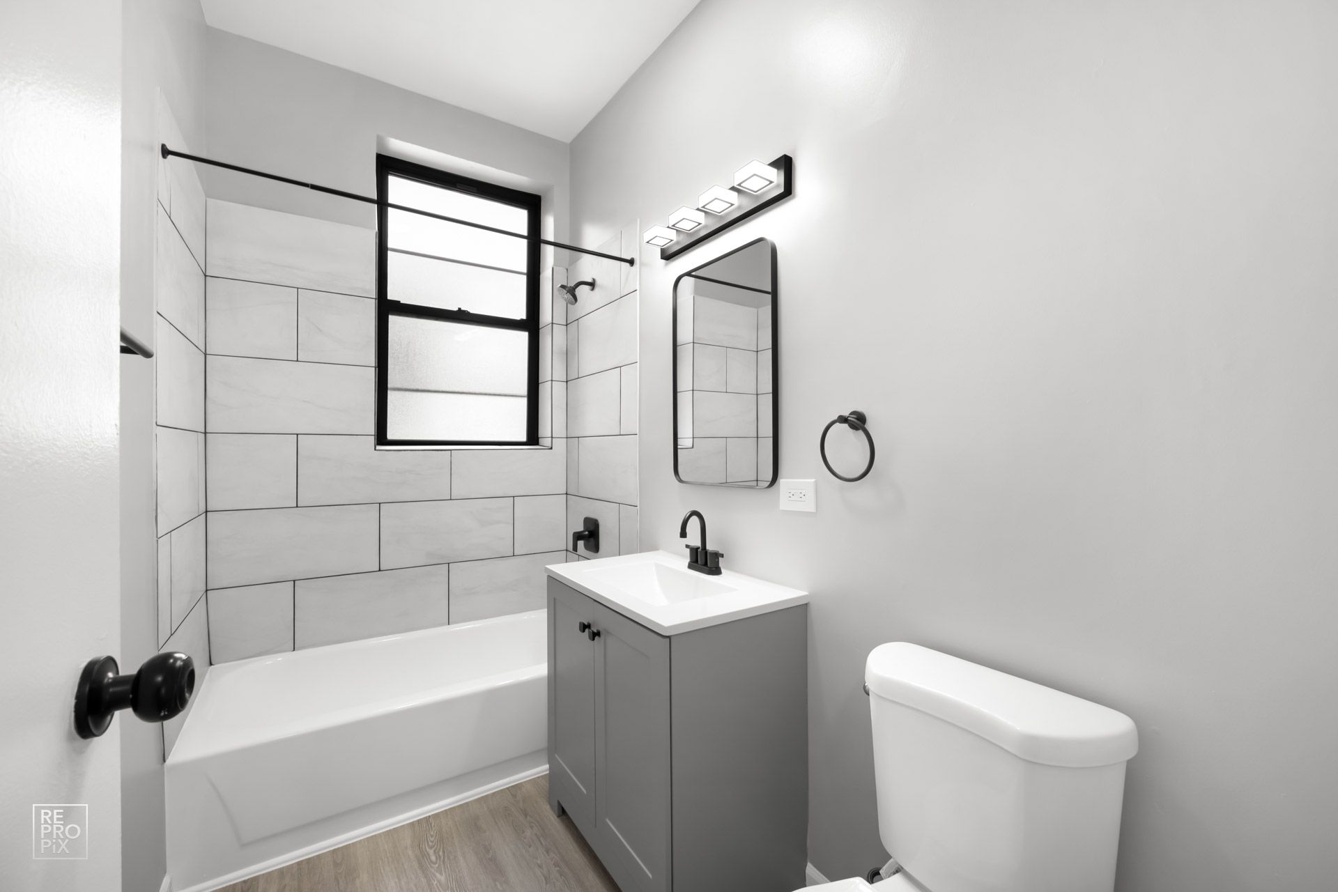 Bathroom with gray walls, white tile shower, gray vanity, and black fixtures.