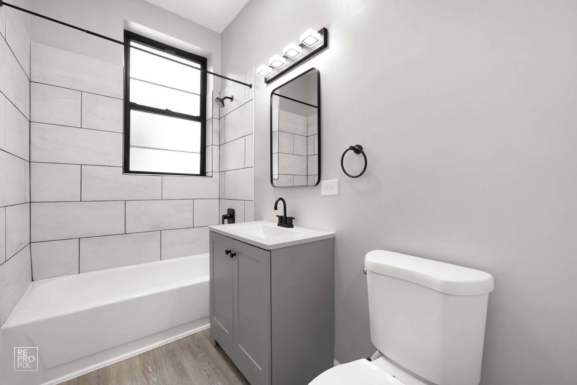Modern bathroom with gray vanity, white toilet, and tile. Black fixtures and trim.