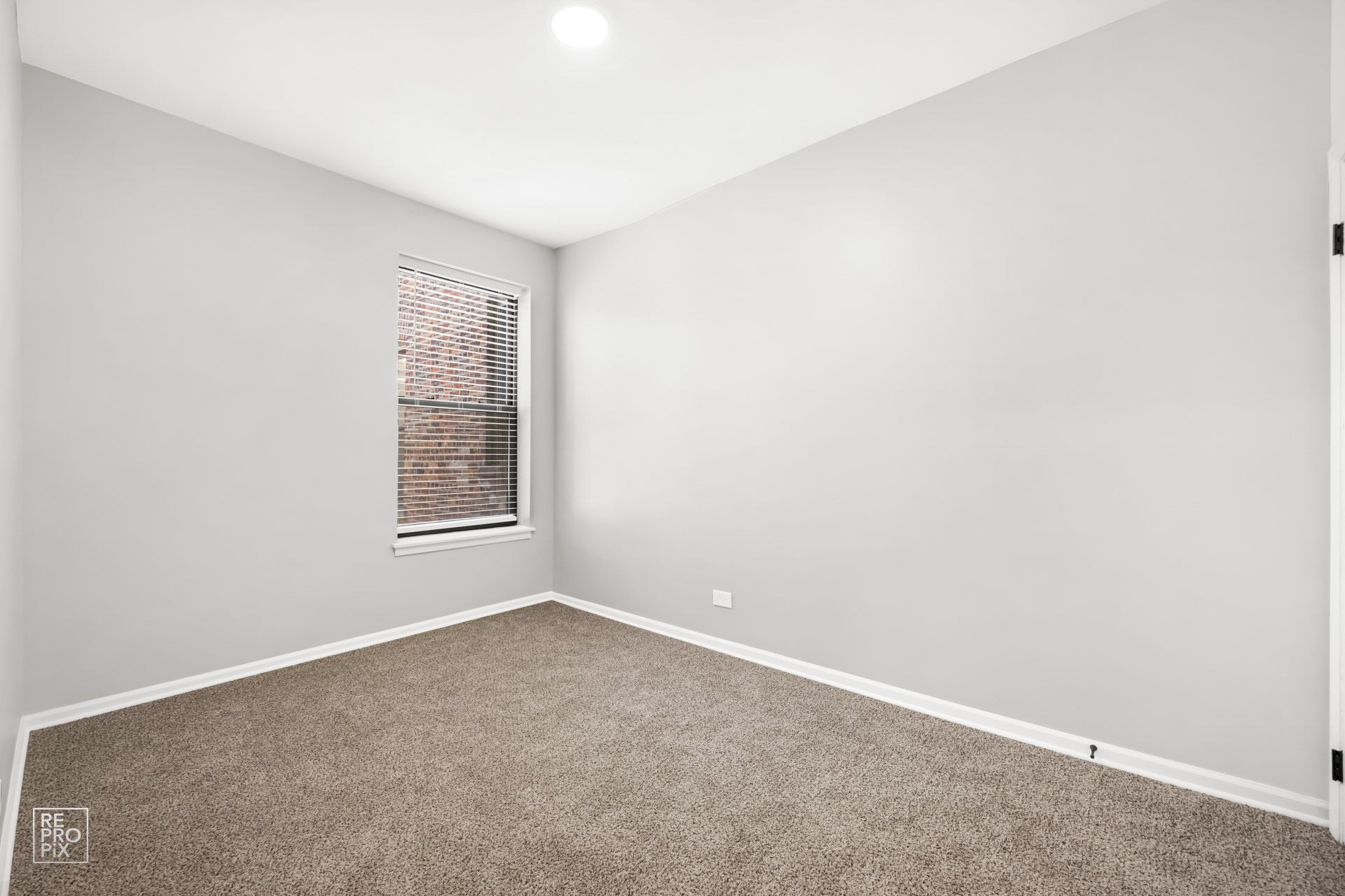 Empty room with gray walls, small window, brown carpet.