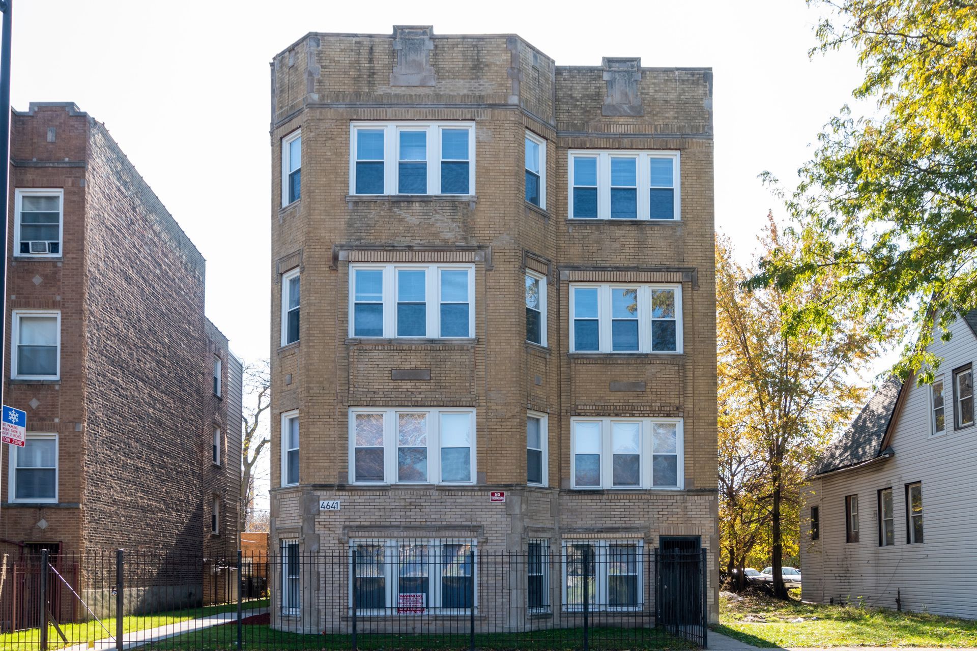 Multi-story tan brick building with multiple windows; fenced yard.