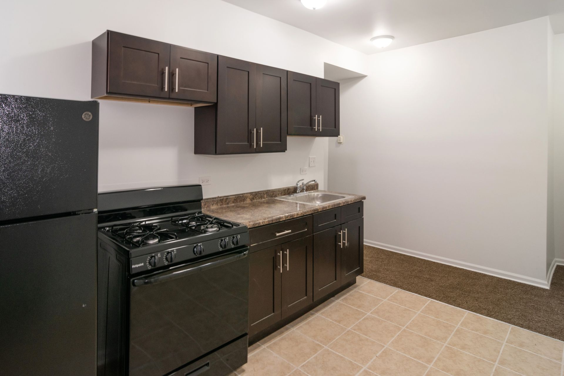 Kitchen with black appliances, dark brown cabinets, and tan countertops and floors.