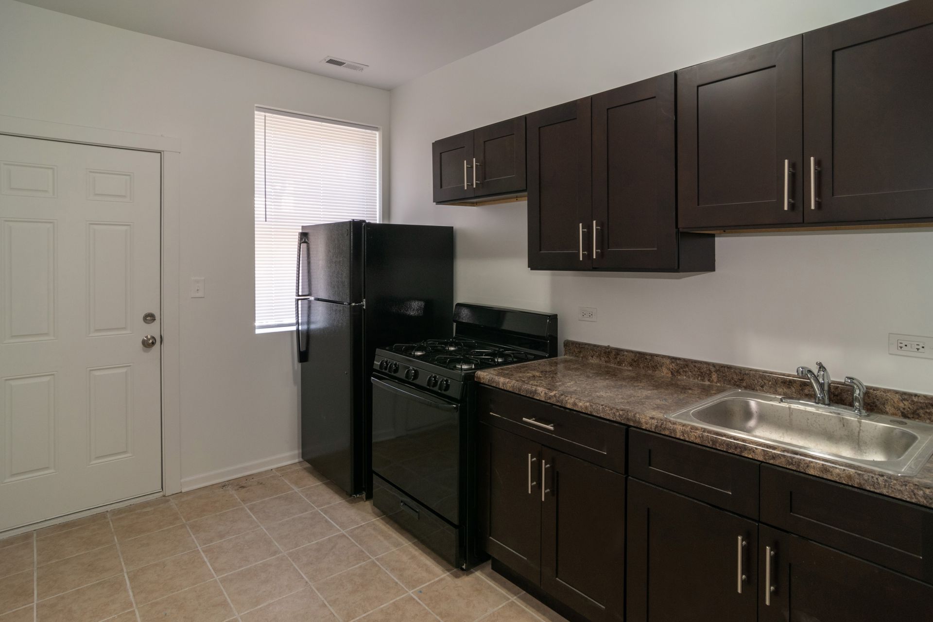 Kitchen with dark brown cabinets, black appliances, and a window.