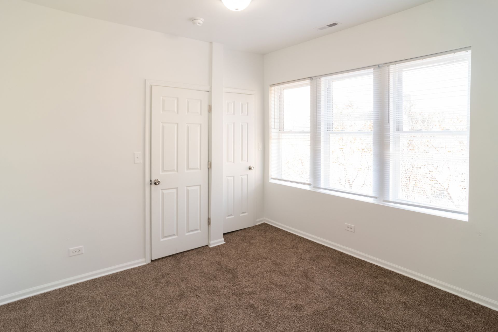 Empty room with brown carpet, white walls, two doors, and a window.