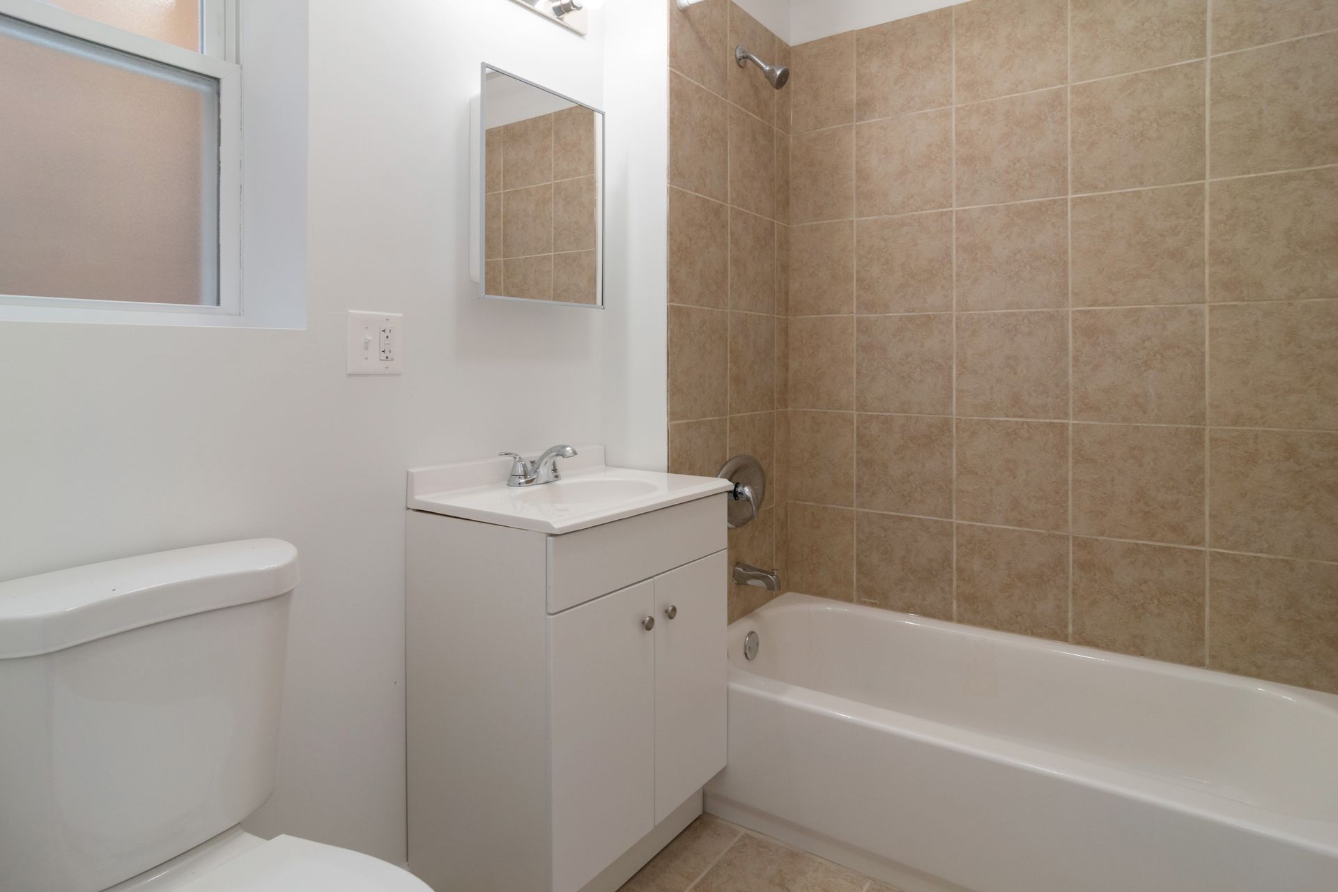 Bathroom with white fixtures, beige tile shower, and vanity.