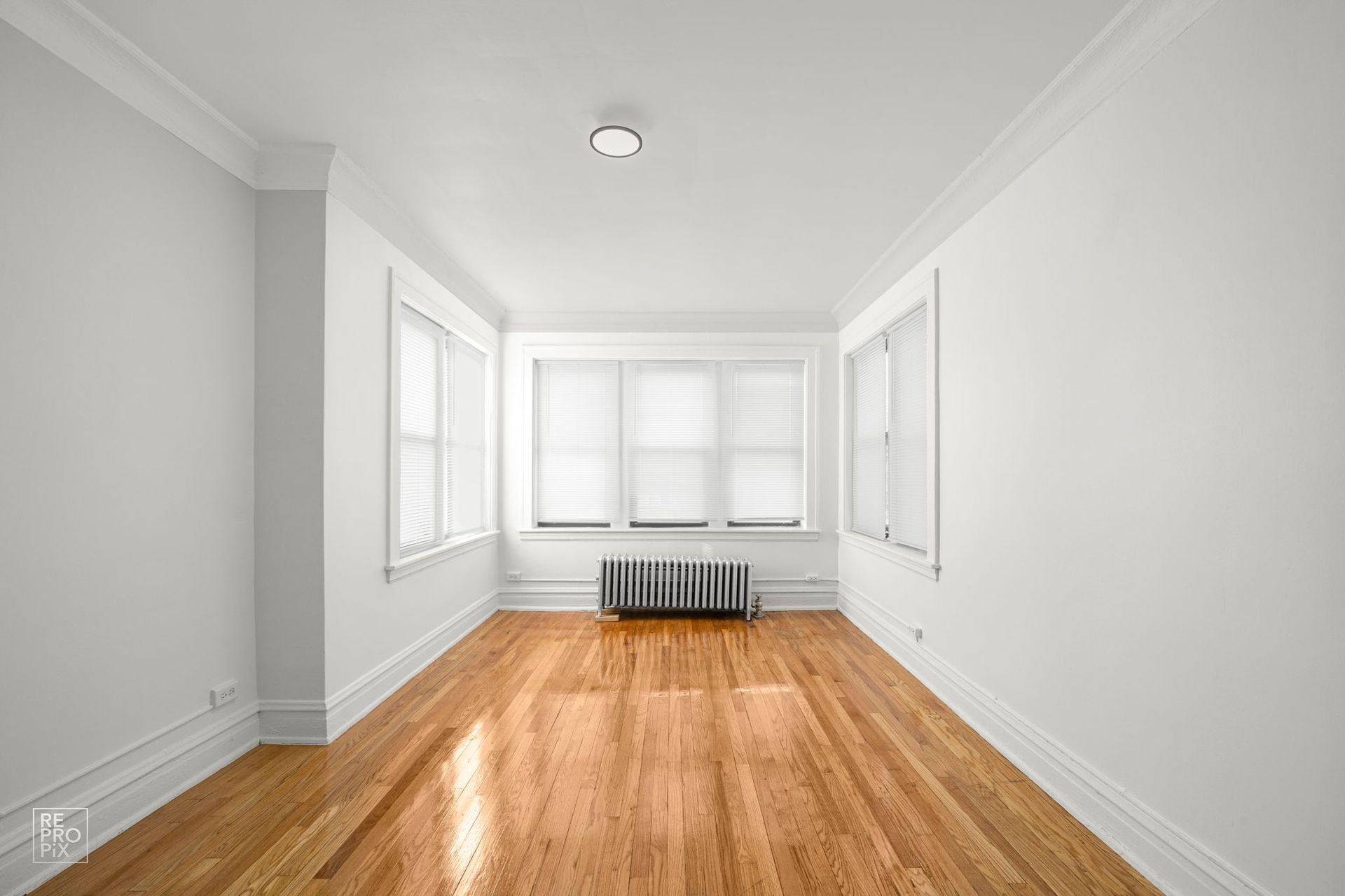 Empty room with hardwood floors, white walls, and three windows with blinds.