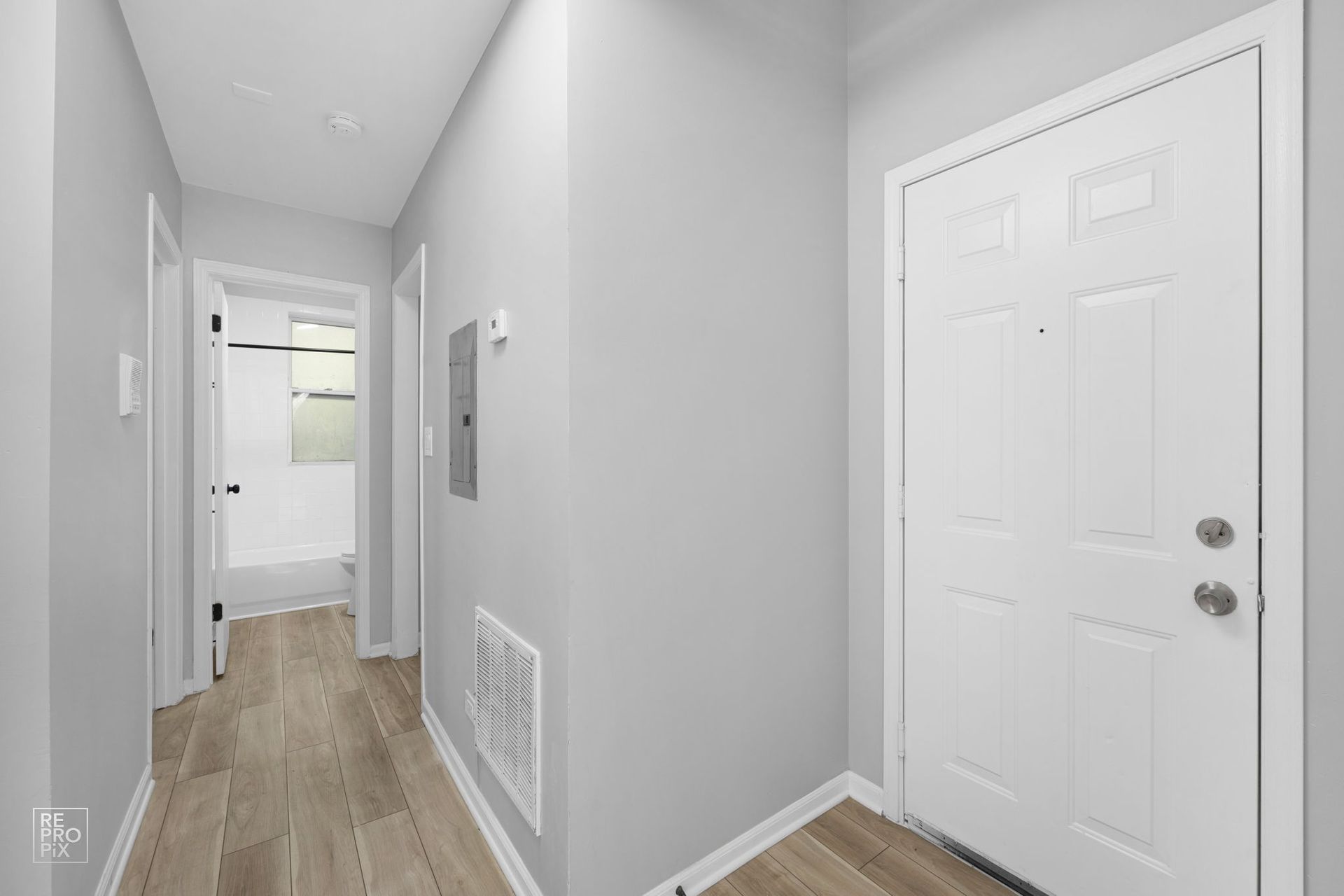Hallway with white door and light gray walls, leading to a bathroom.