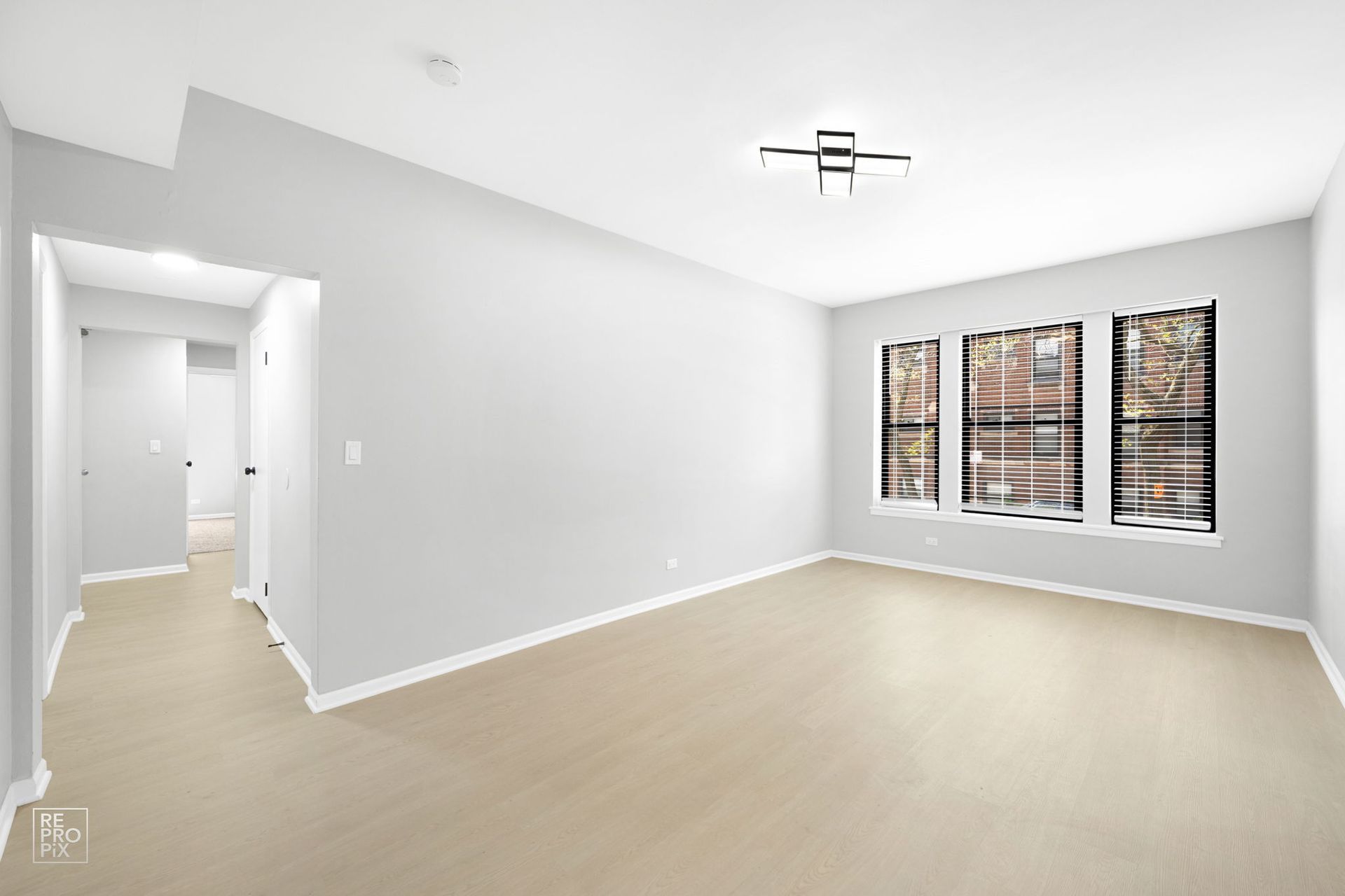 Empty room with three windows, a hallway entrance, and beige carpet. Light gray walls and white ceiling.