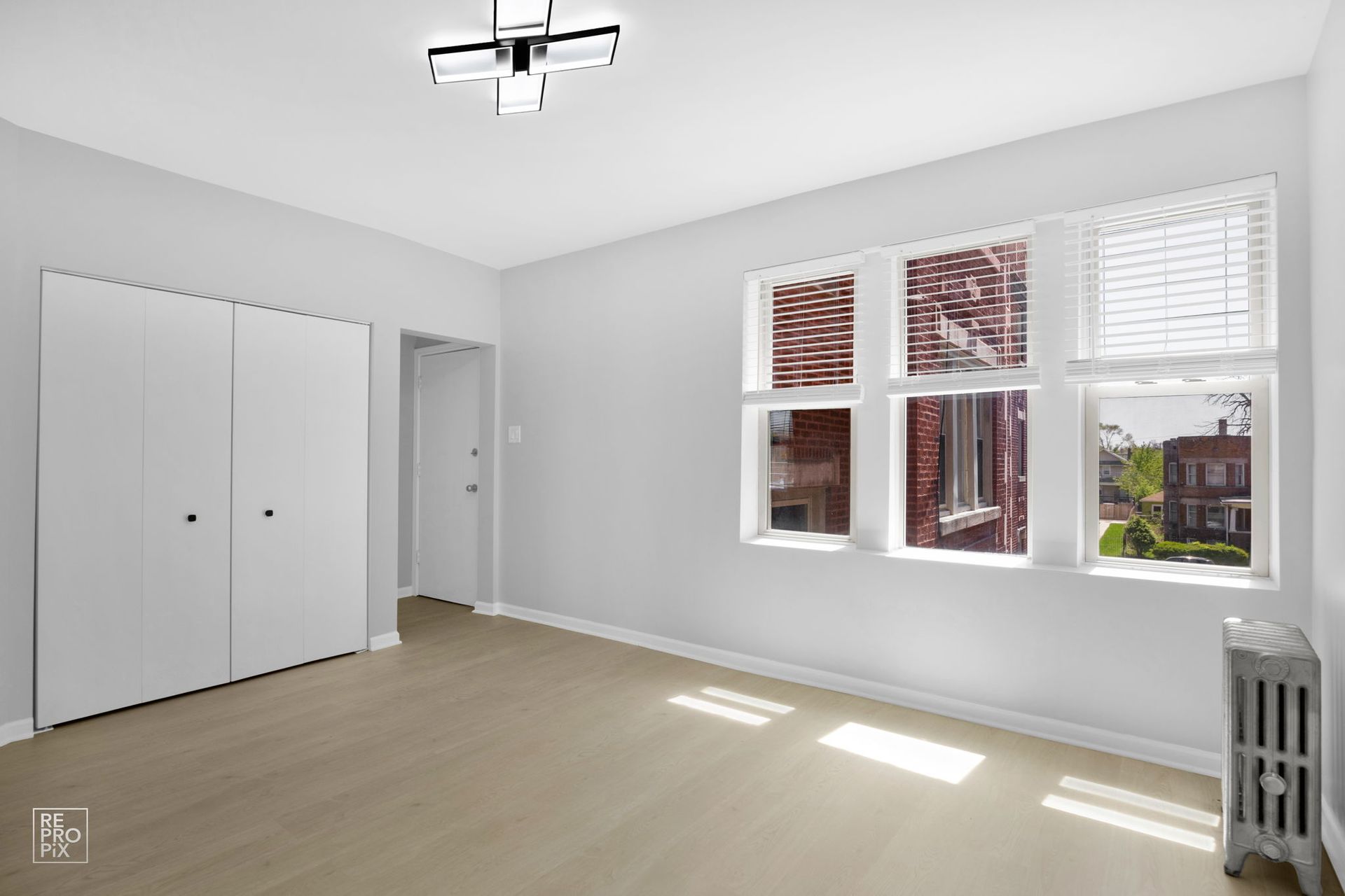 Empty room with light-colored walls, wood-look floor, windows, and a closet.