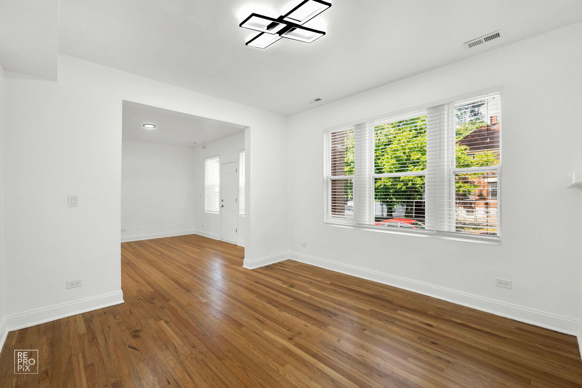 Empty room with hardwood floors, large window, and recessed doorway.