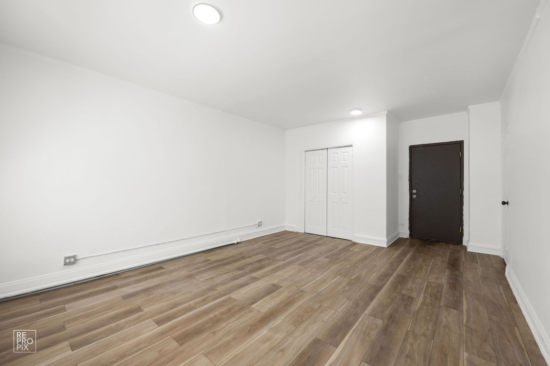 Empty room with wood floors, white walls, two closets, and a dark door.