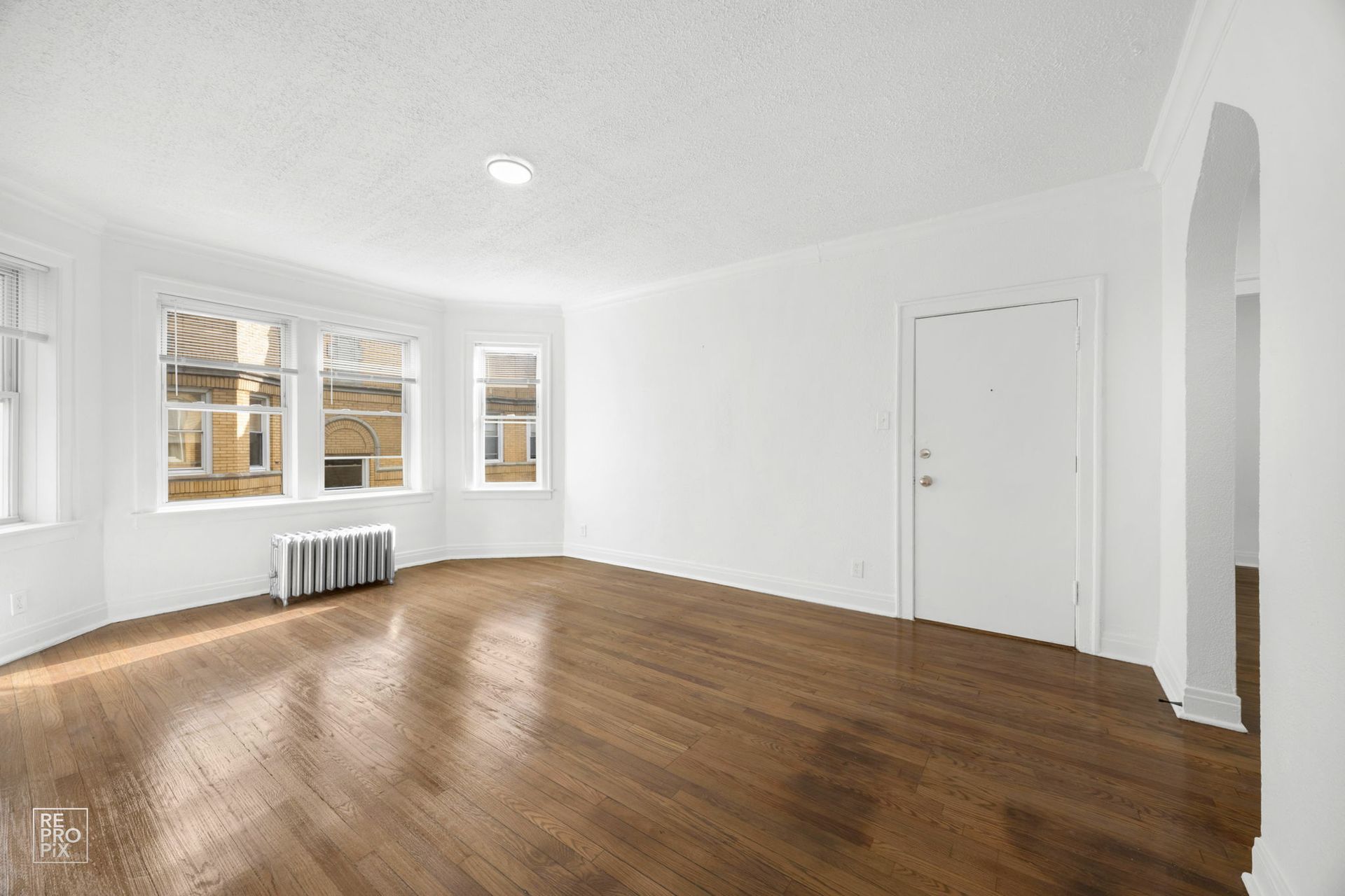 Empty living room with wood floors, white walls, and a window.