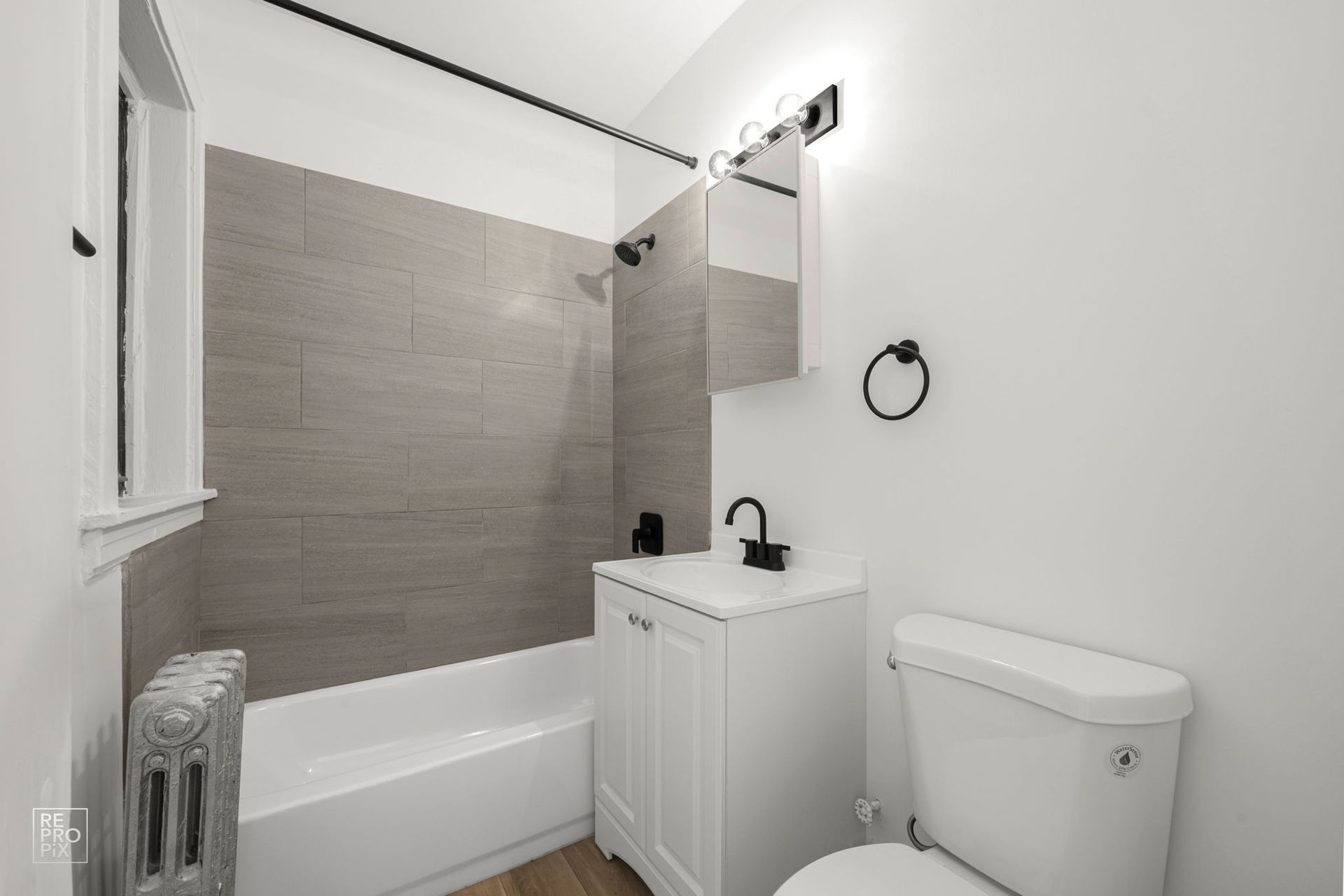 Small white bathroom with gray tile shower surround and black fixtures.