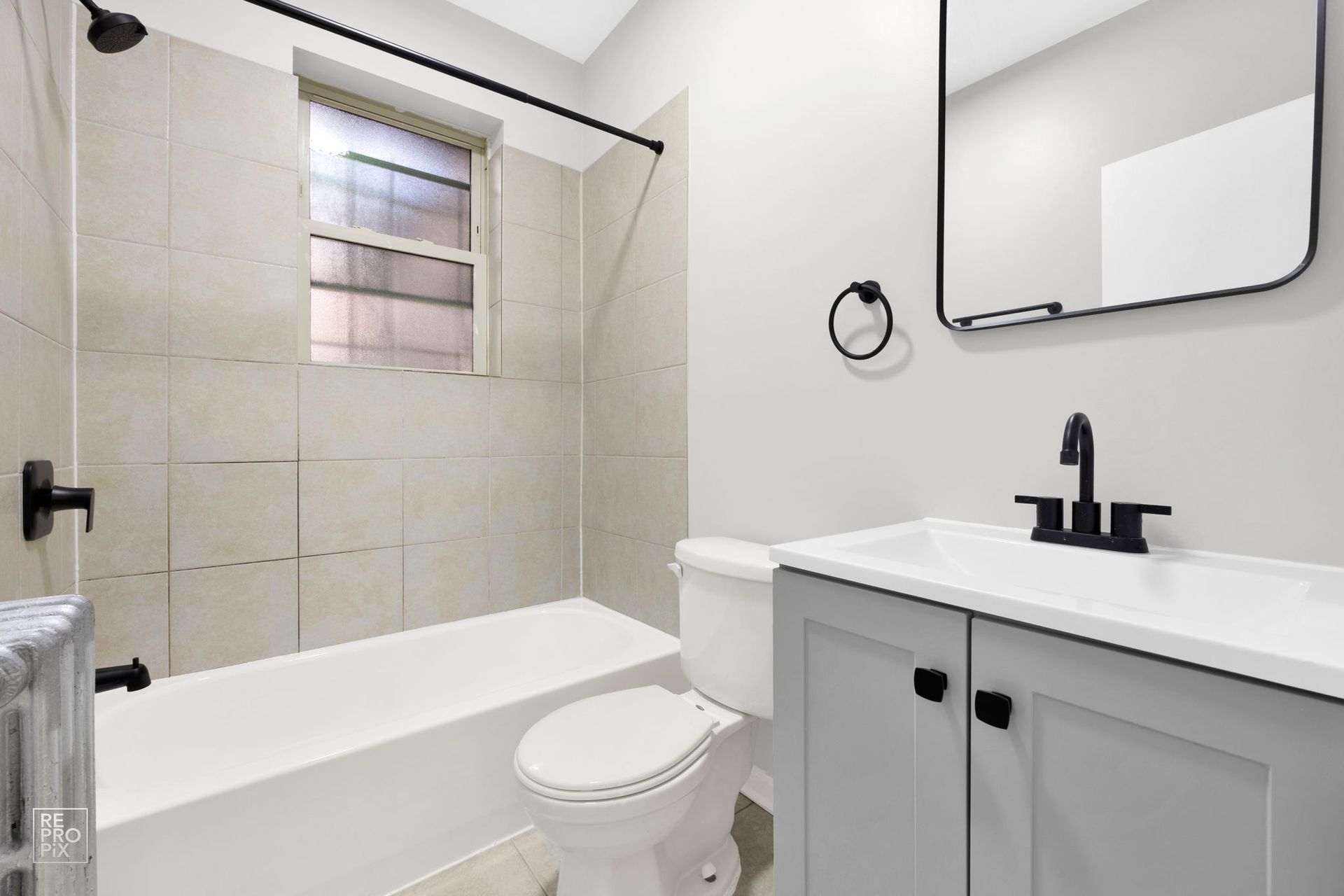 Bathroom with gray vanity, white toilet, and beige tile shower. Black fixtures.