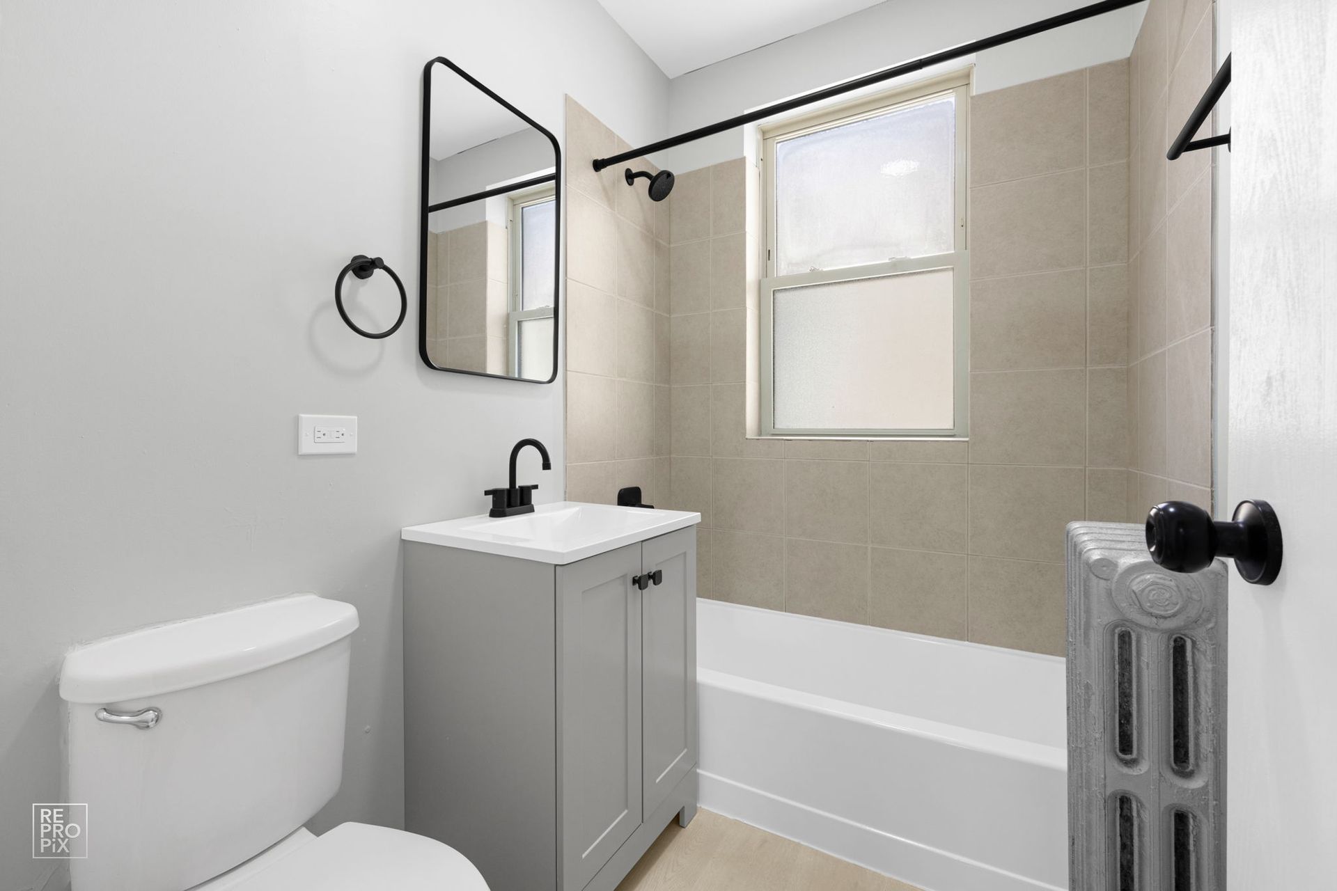 Bathroom with light gray walls, a white toilet, gray vanity, and beige tiled shower.