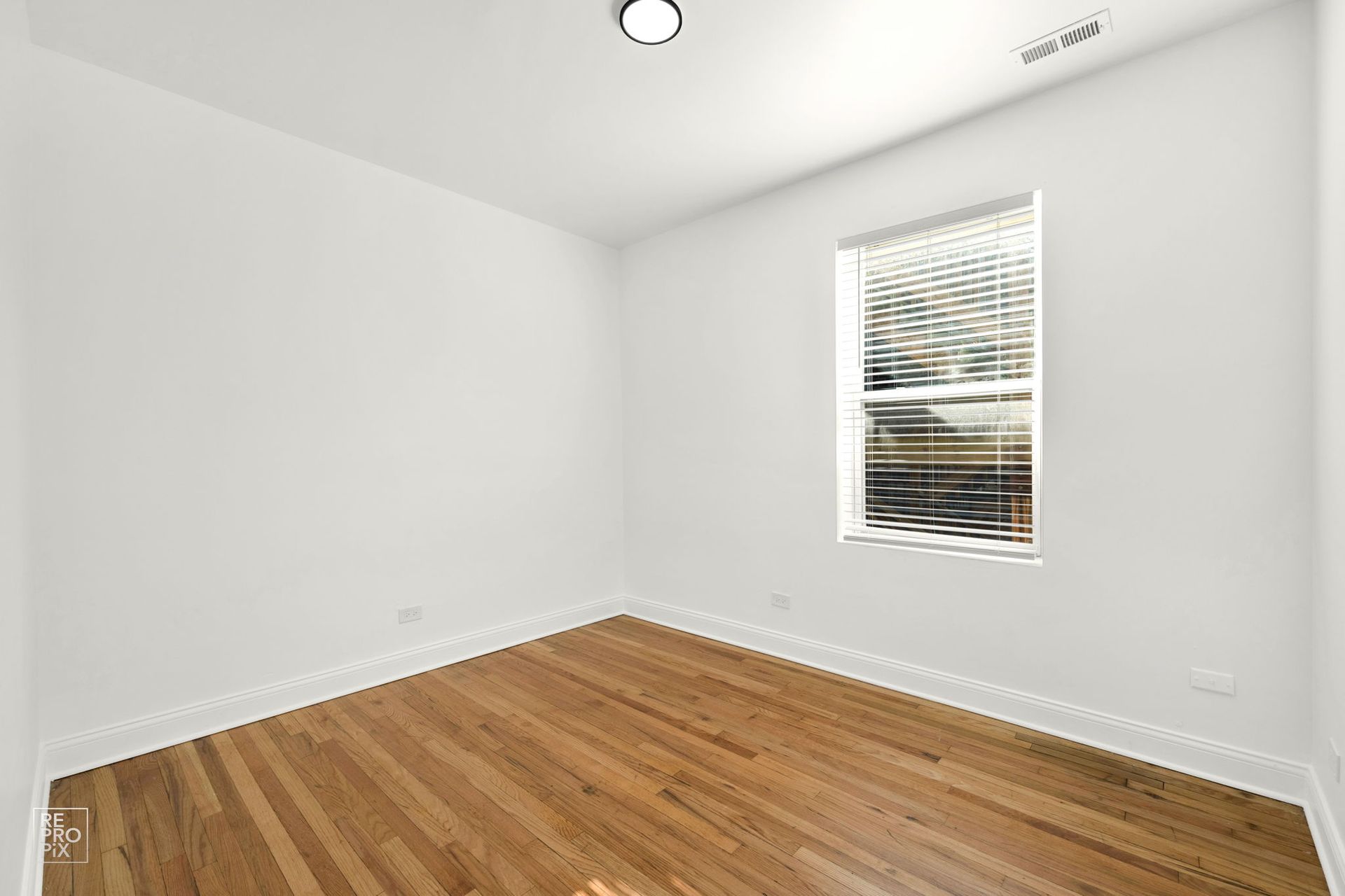 Empty room with hardwood floor, white walls, and a window with blinds.