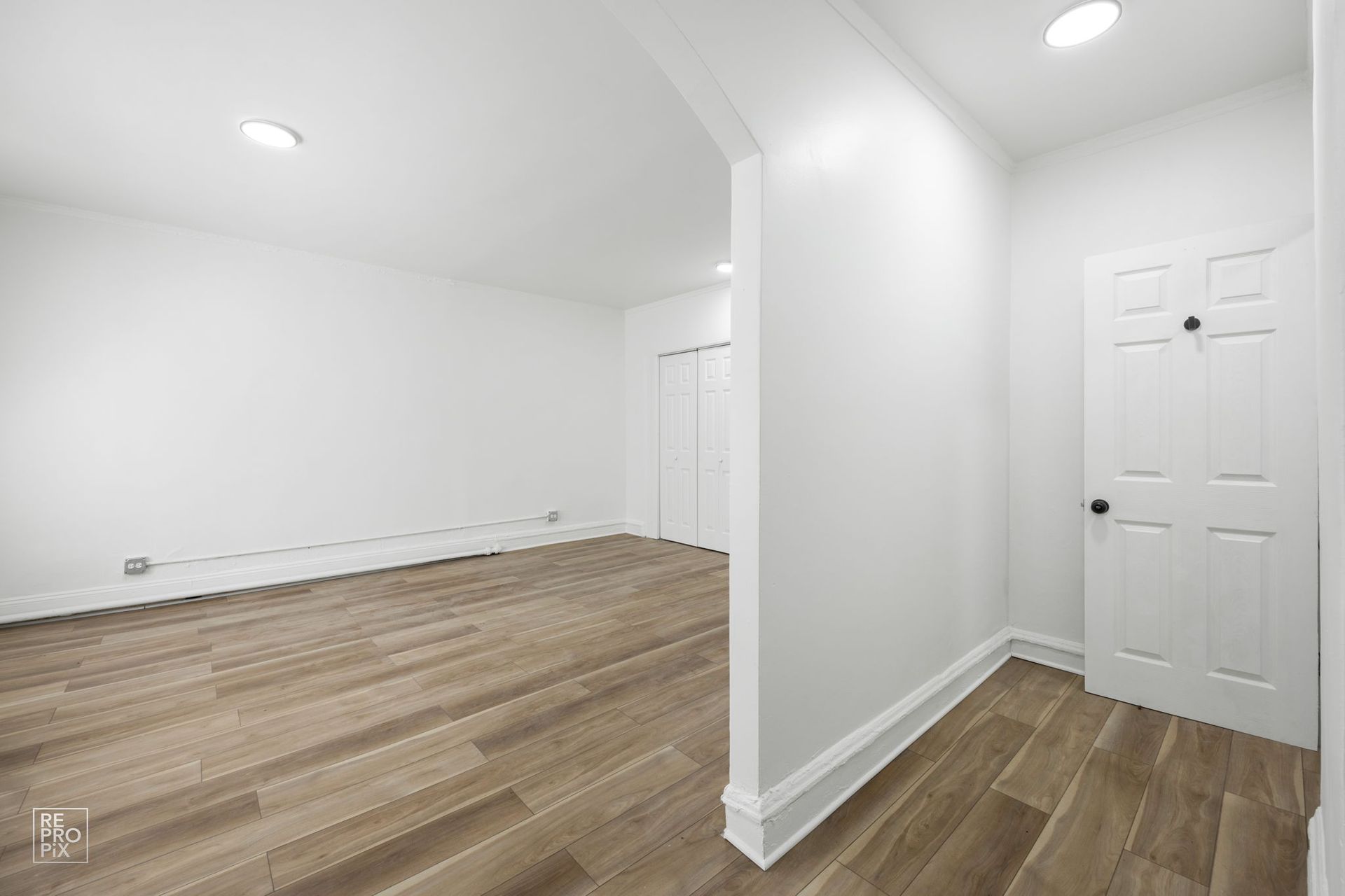 Empty room with light wood floors, white walls, and a doorway leading to a hallway.