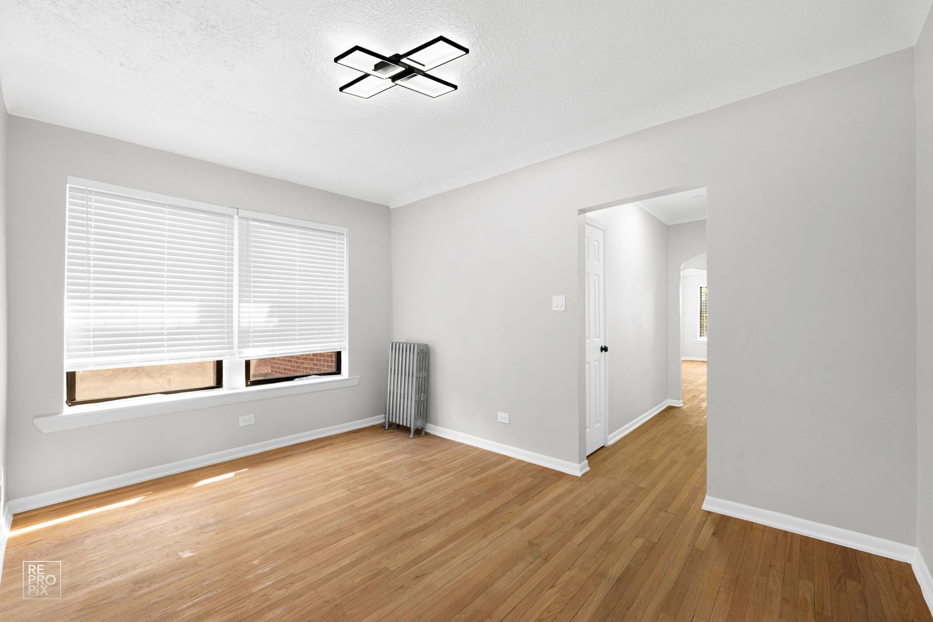 Empty room with wood floors, blinds, and a doorway, painted gray, with modern ceiling light.