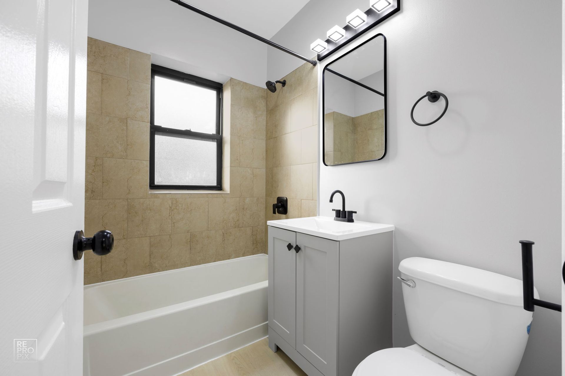 Bathroom with tub, window, toilet, vanity, and black accents; tan and white color scheme.