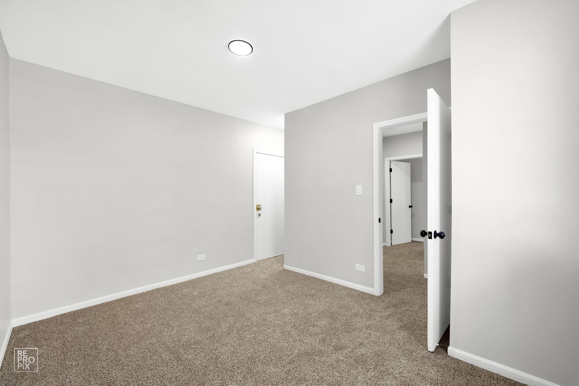 Empty room with light gray walls, carpet, and an open doorway to another room.
