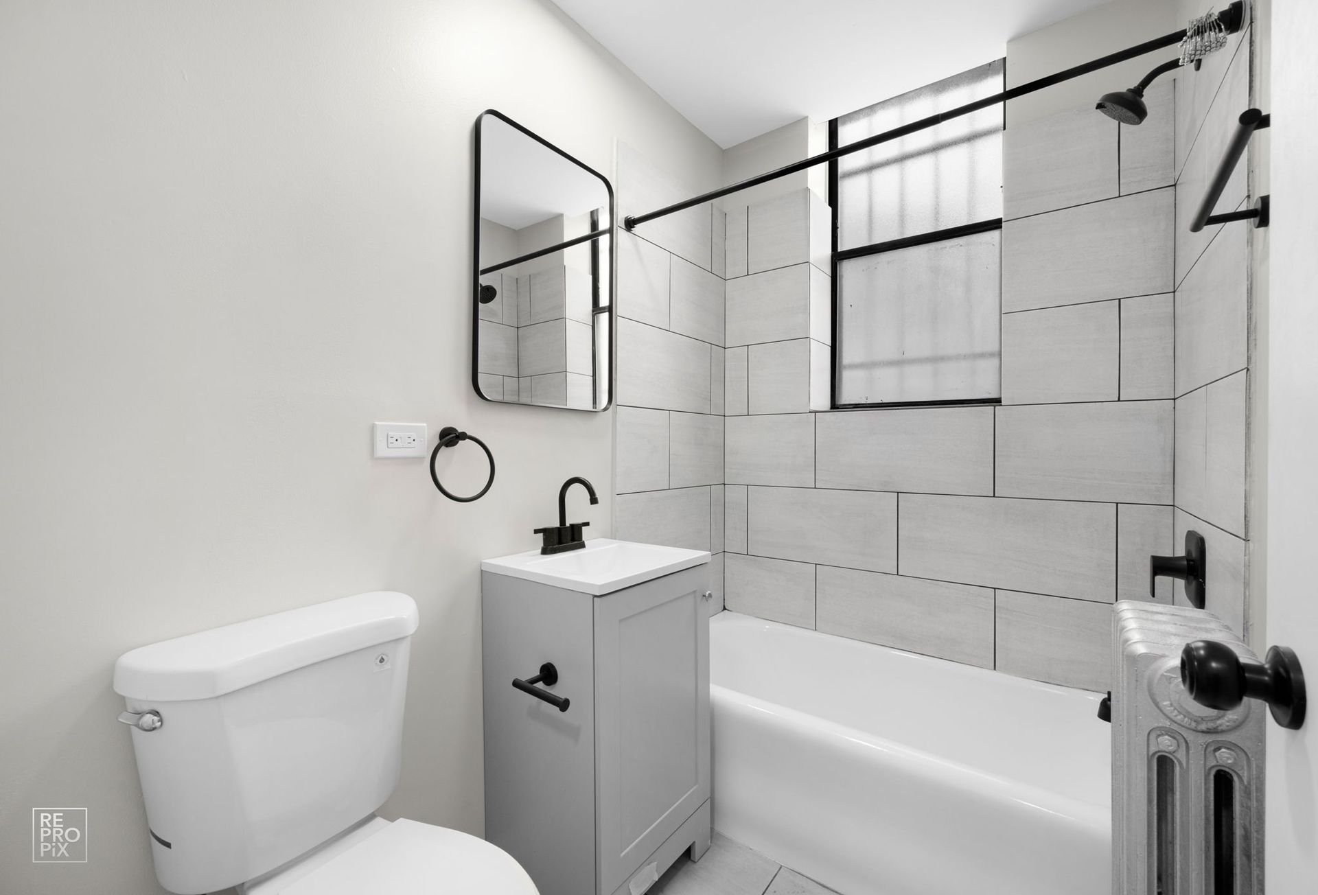 Bathroom with white tile, gray vanity, and black fixtures.