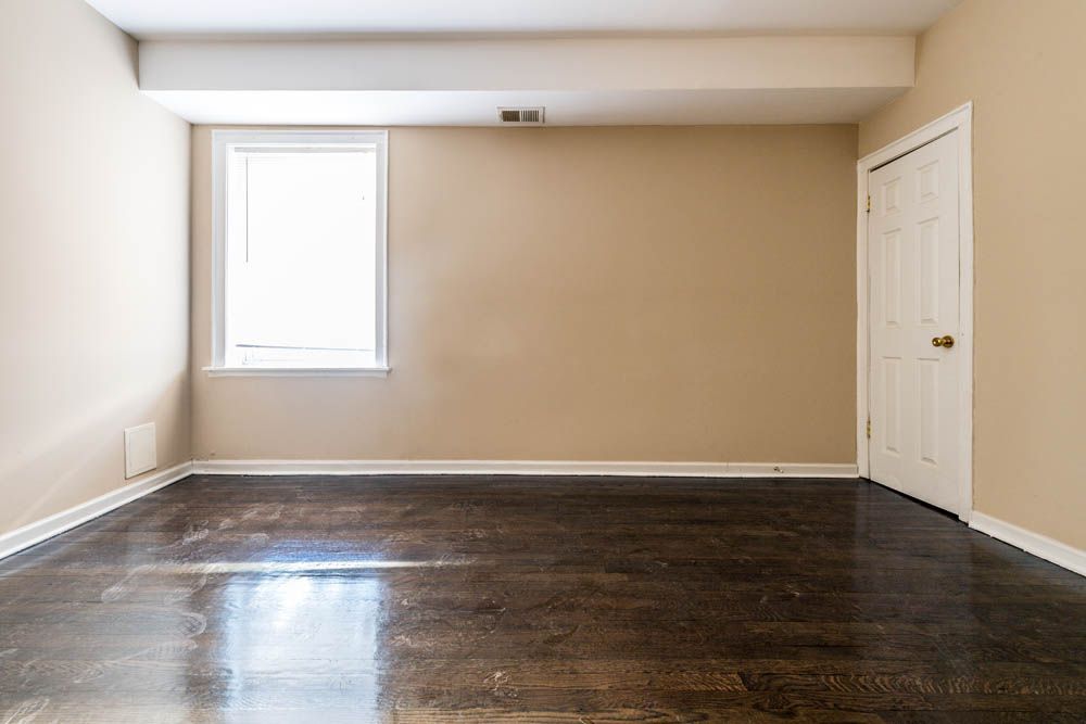 Empty room with hardwood floors, a window, and a door, painted in neutral tones.