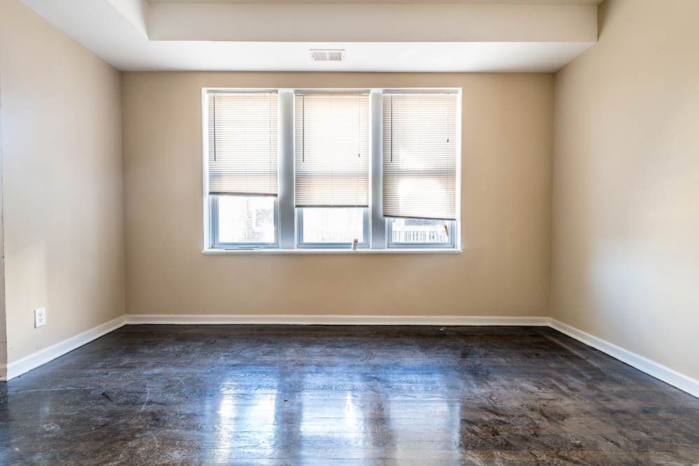 Empty room with three windows, beige walls, and dark flooring.