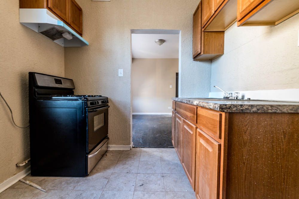 Kitchen with stove, cabinets, and a doorway leading to a room with dark flooring.