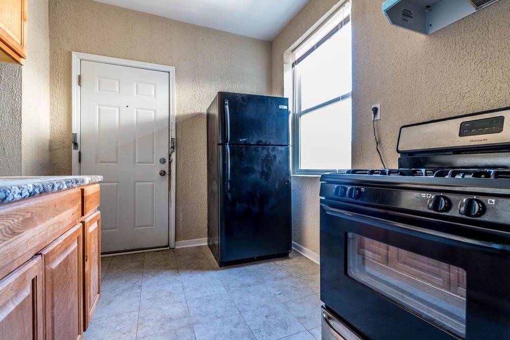A kitchen with a black refrigerator, a stove, a door, a window, and wooden cabinets.