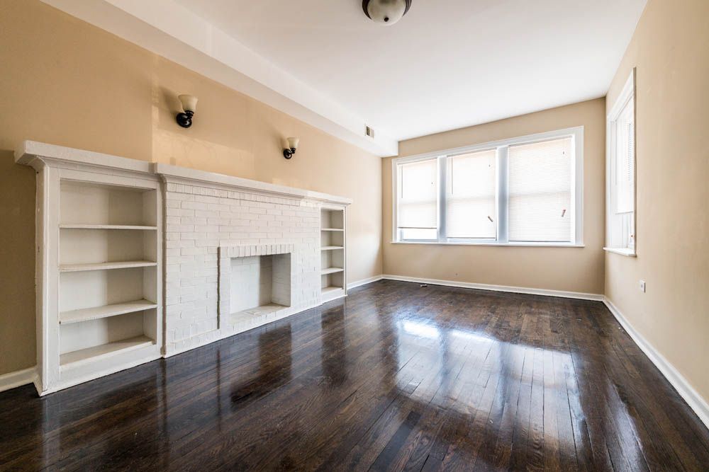 Empty living room with dark wood floor, fireplace, and built-in bookshelves.