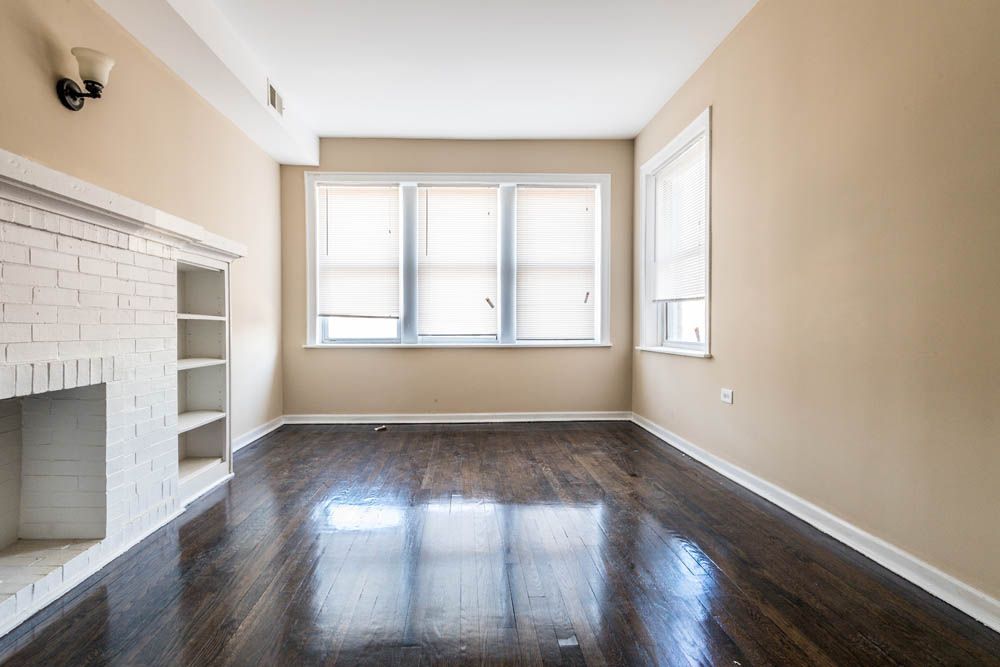 Empty living room with dark wood floor, white fireplace, and beige walls.