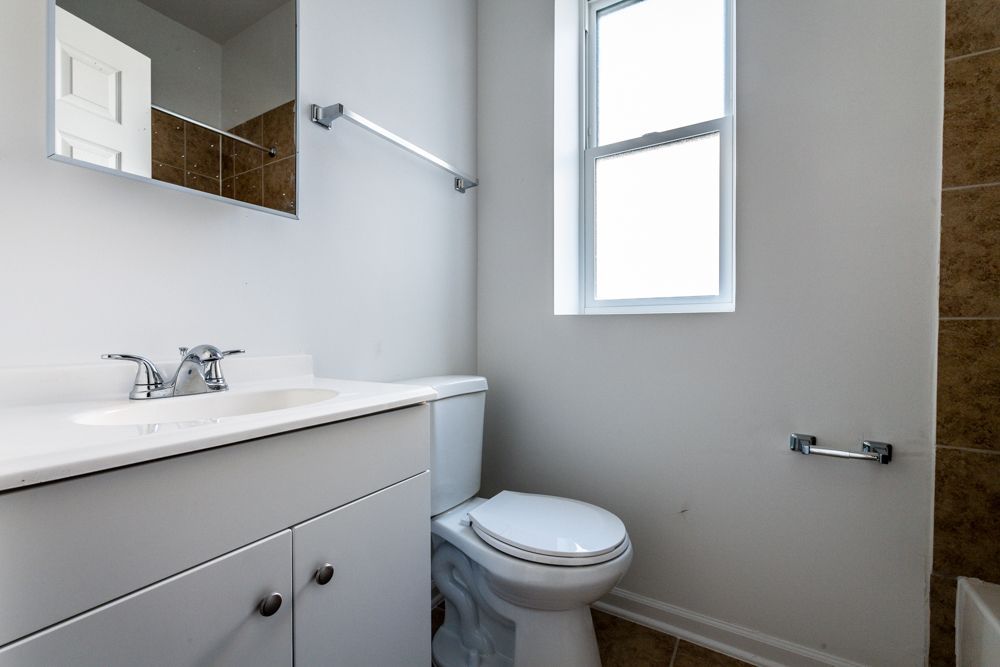 White bathroom with a toilet, sink, mirror, and window.