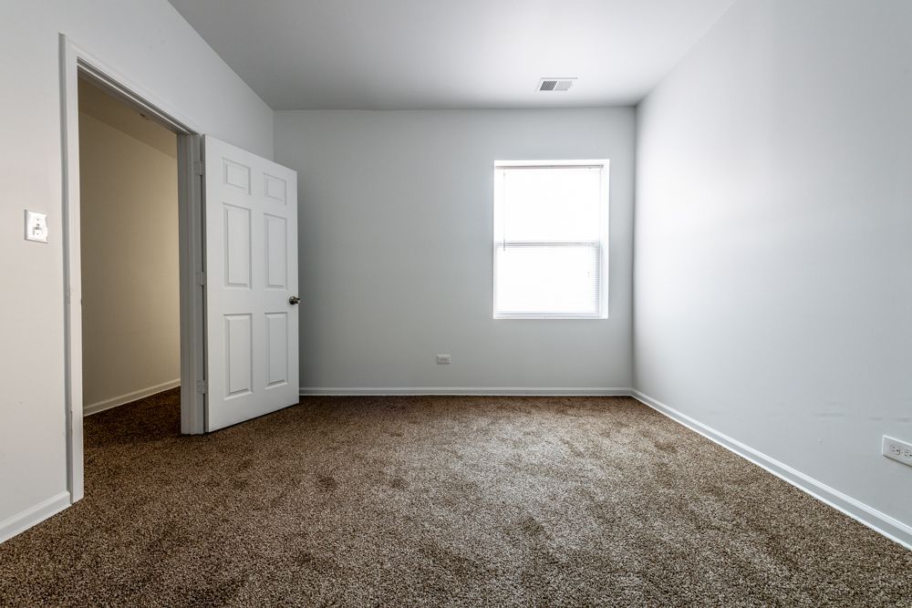 Empty room with brown carpet, white walls, open door, and window.