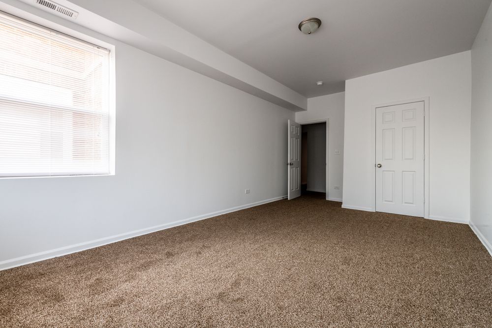 Empty room with beige carpet, white walls, a window, and two doors.