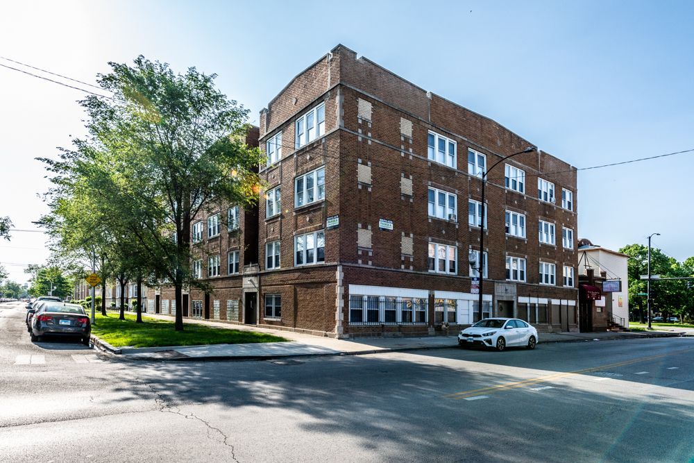 Brick apartment building on a corner lot; parked cars, trees, overcast sky.