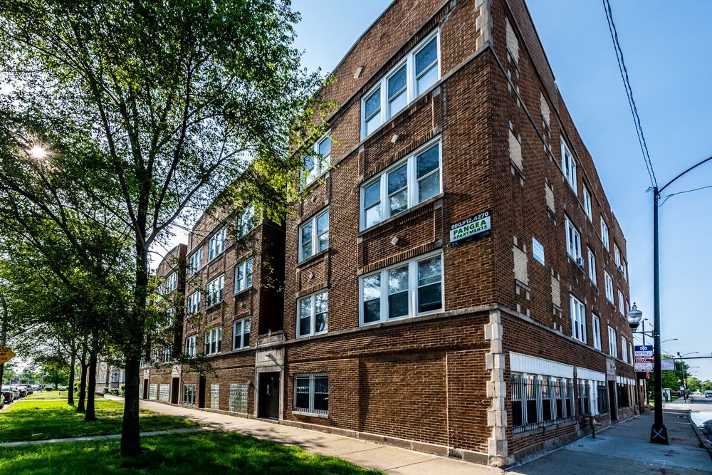 Brick apartment building with multiple windows, trees, and a street sign on a sunny day.