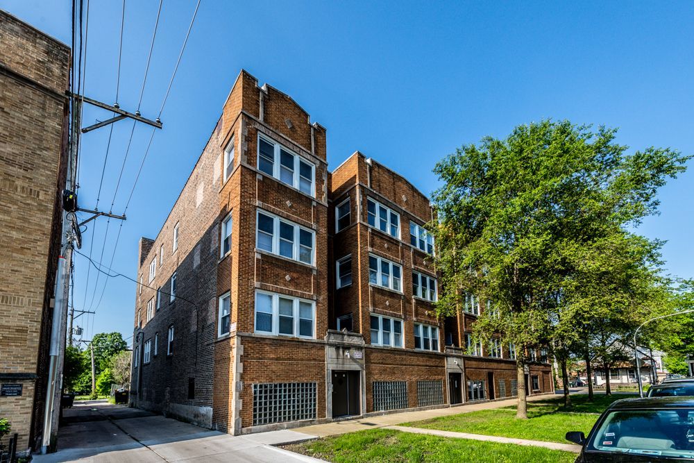Brick apartment building on a sunny day with green trees and blue sky.