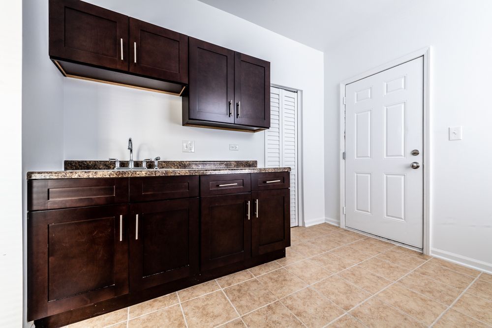 Dark brown kitchen cabinets with a sink and a white door in a well-lit room.