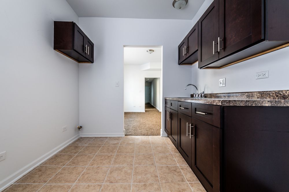 Kitchen with dark brown cabinets, a sink, and a doorway leading to a hallway. Light-colored tile floors.