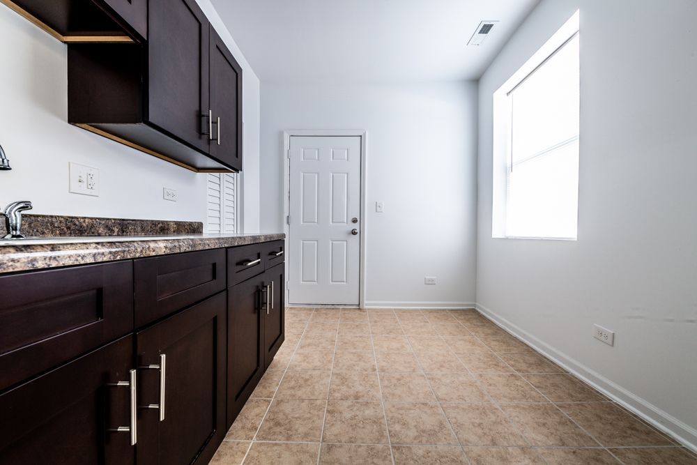 Kitchen with dark brown cabinets, granite countertop, white door, and window.