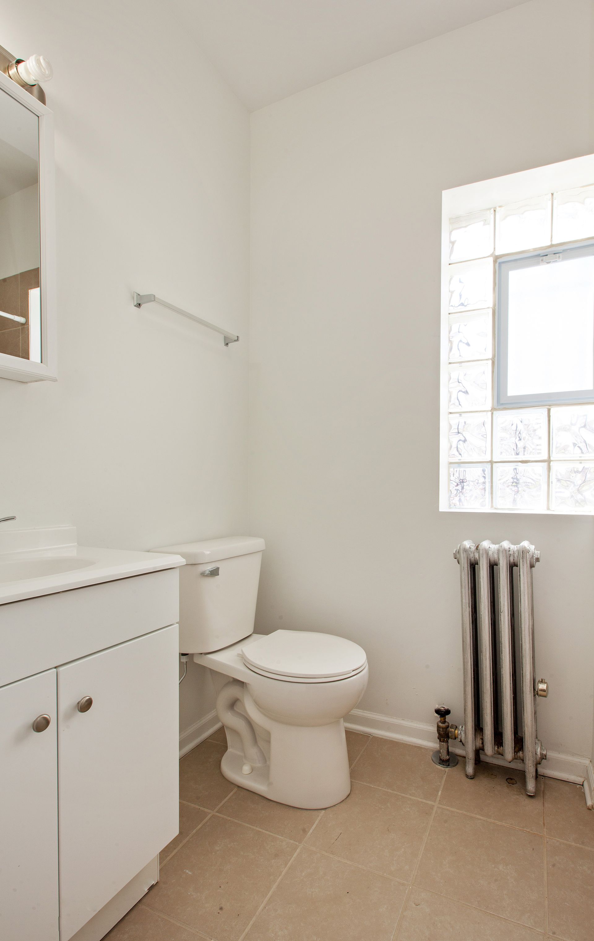 A small, white bathroom with a toilet, sink, and radiator. A window provides natural light.
