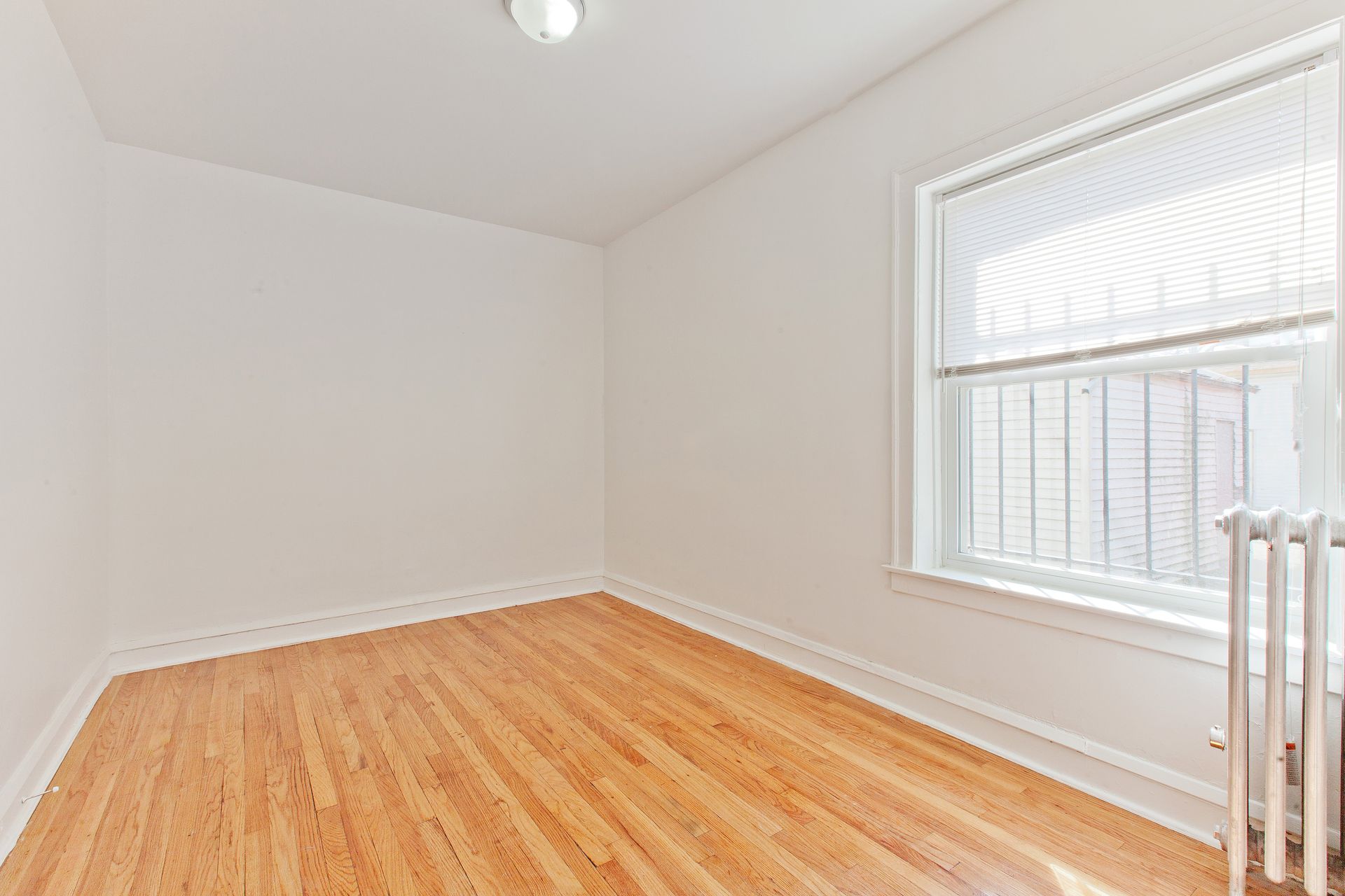 Empty room with hardwood floors, white walls, and a window with a blind.