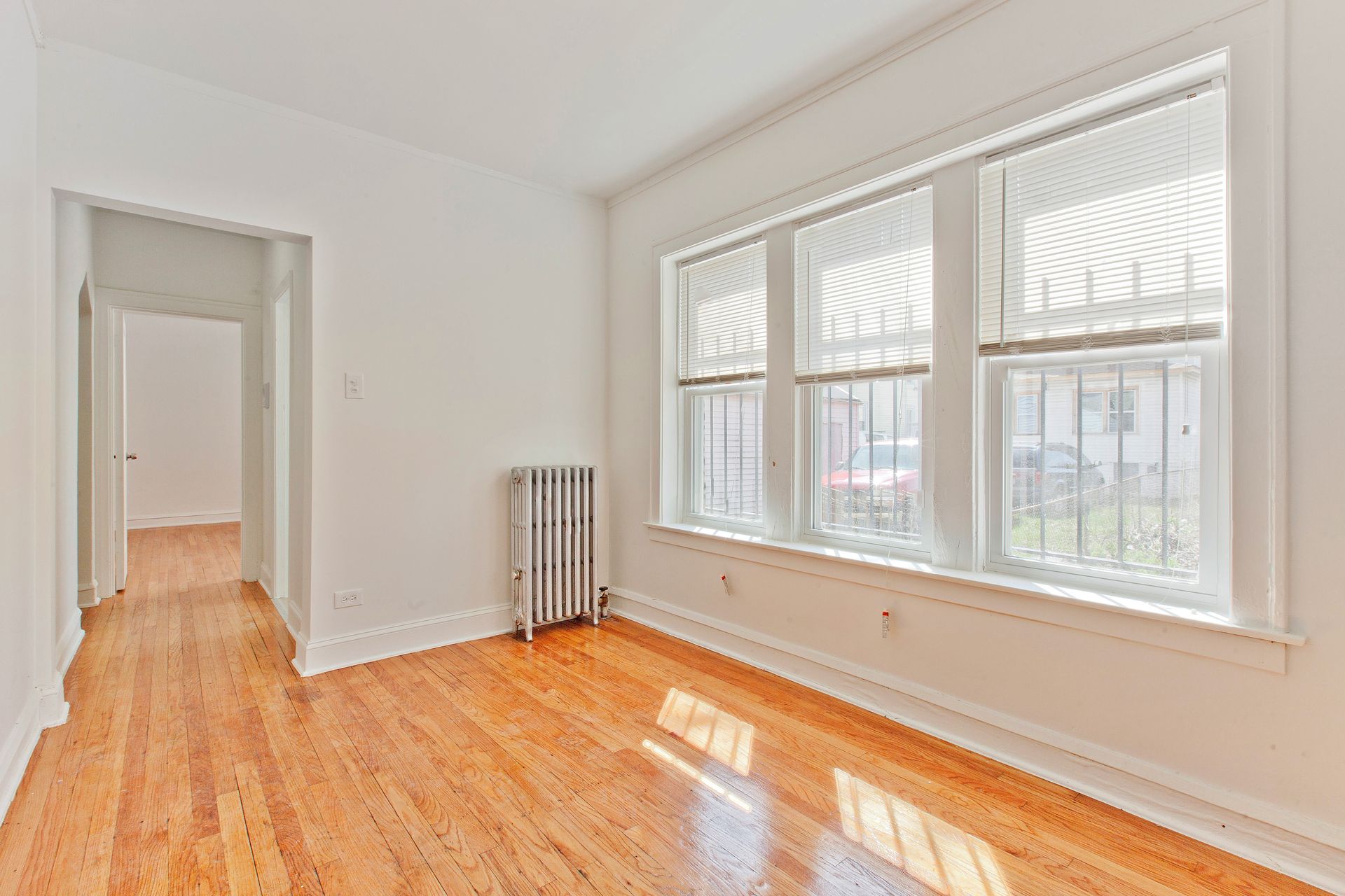 Empty room with hardwood floors, a radiator, and a three-window wall with window coverings.