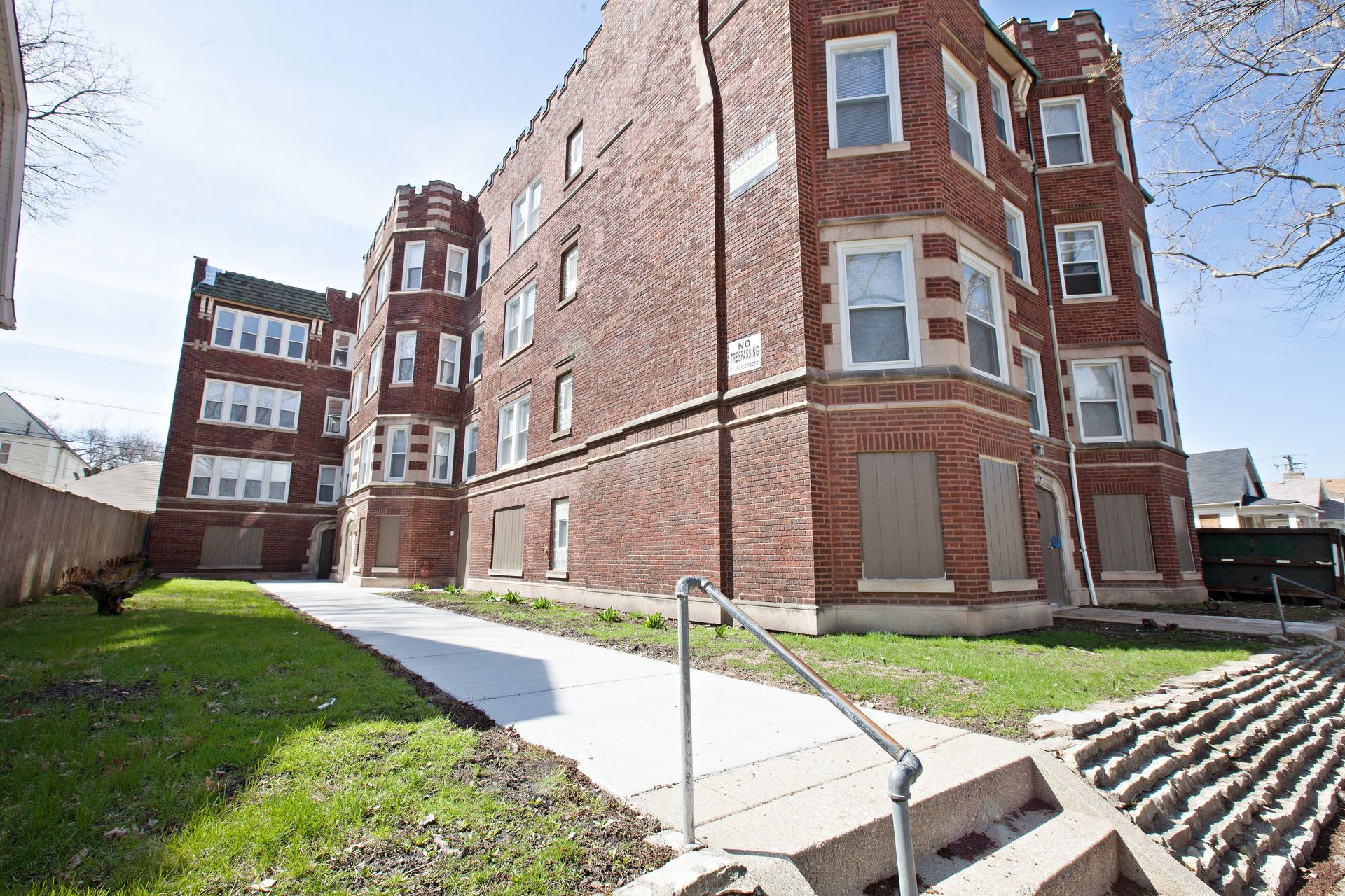 Red brick apartment buildings with boarded-up windows and a concrete pathway leading to the entrance.